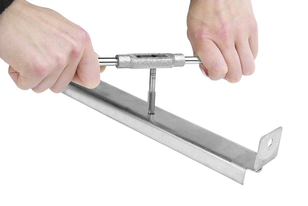 Eine Person benutzt einen Gewindebohrer, um in ein Metallprofil ein Innengewinde zu schneiden. Hände halten das Werkzeug, das in das Metall gedreht wird.