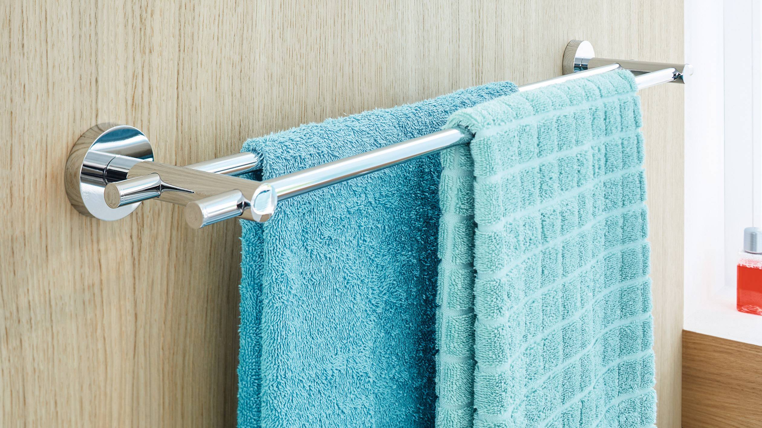 Deux serviettes turquoises sont suspendues côte à côte à une barre argentée devant un mur en bois.