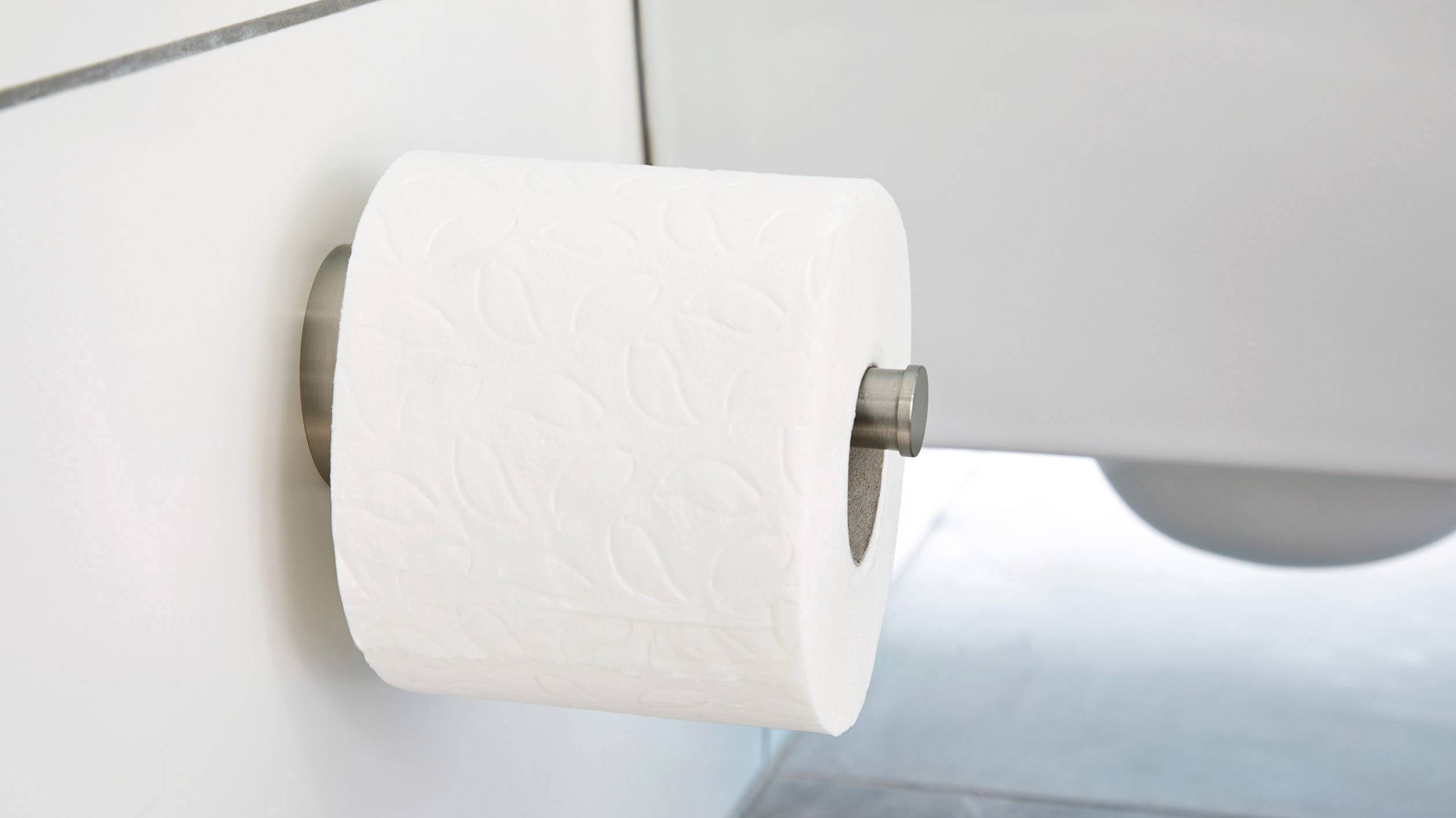 Rouleau de papier toilette décoratif à motif de feuilles, fixé sur un support mural dans une salle de bain lumineuse.