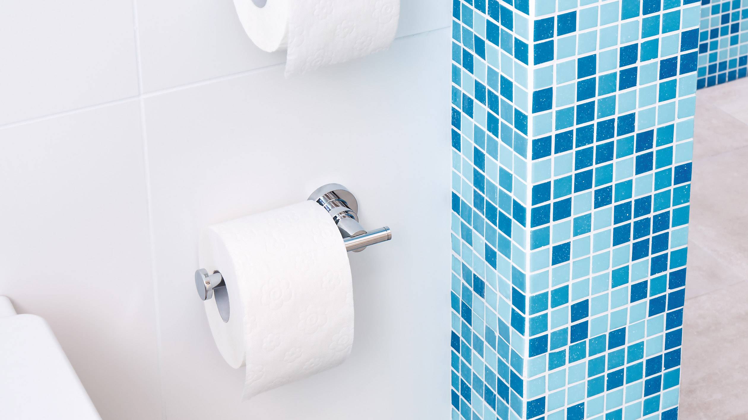 Support de papier toilette sur un mur carrelé bleu. Deux rouleaux sont visibles, l'un est en cours d'utilisation, l'autre servant de rechange.