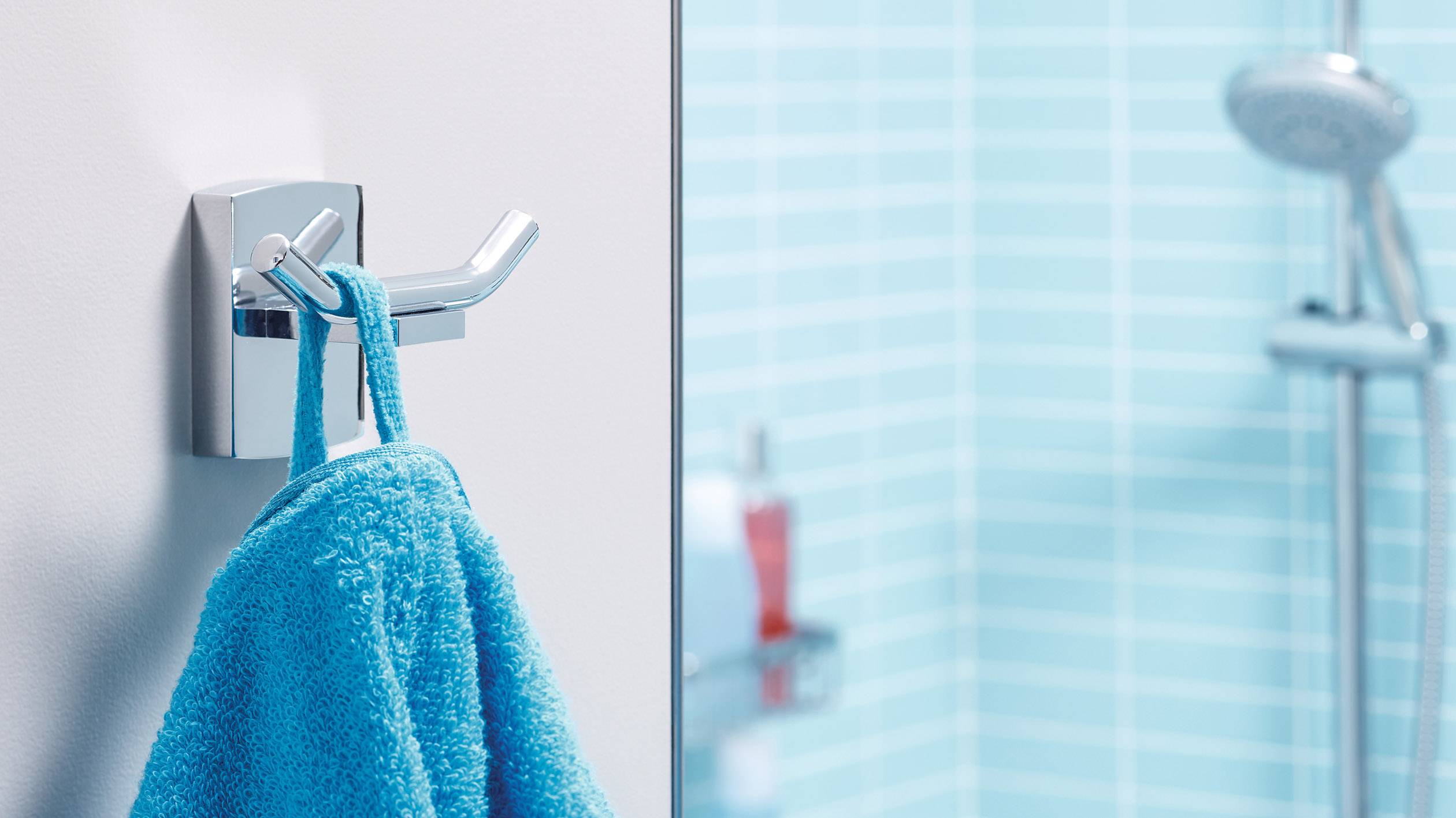 Une serviette bleue est suspendue à un crochet argenté devant une douche aux carreaux bleus.