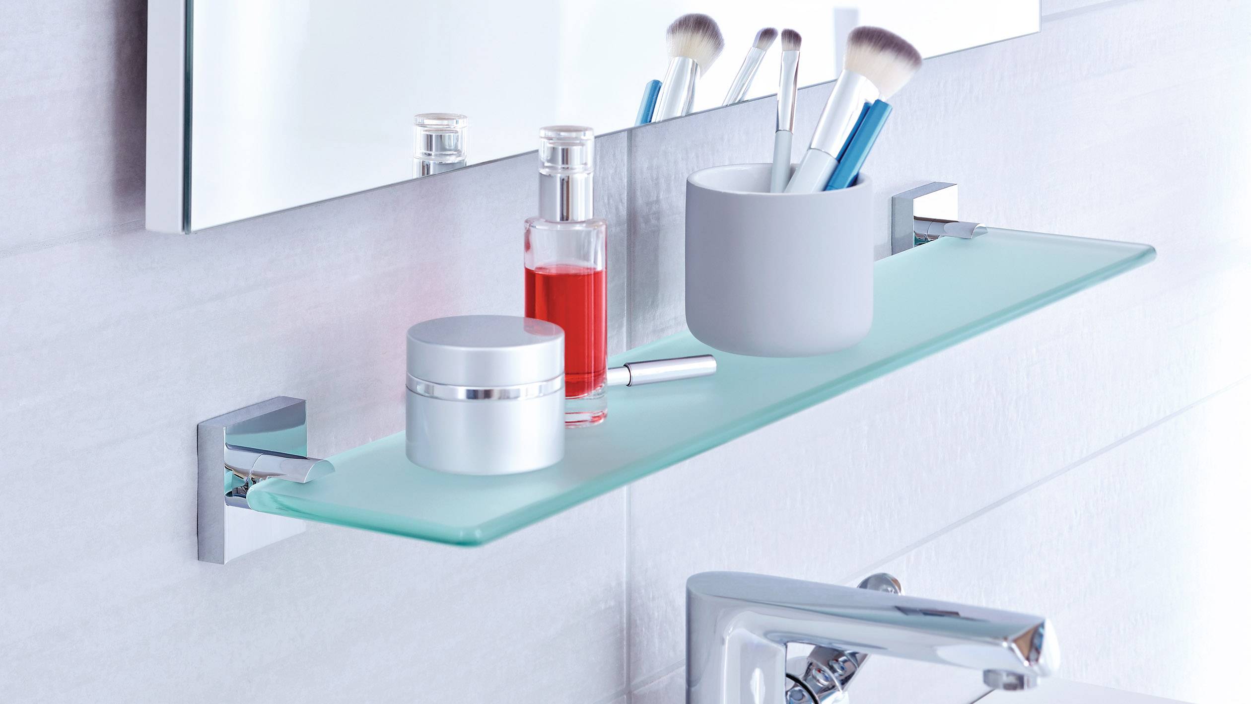 Un étagère de salle de bain moderne en verre avec des articles de cosmétique tels que des brosses, des pots de crème et un flacon de parfum.