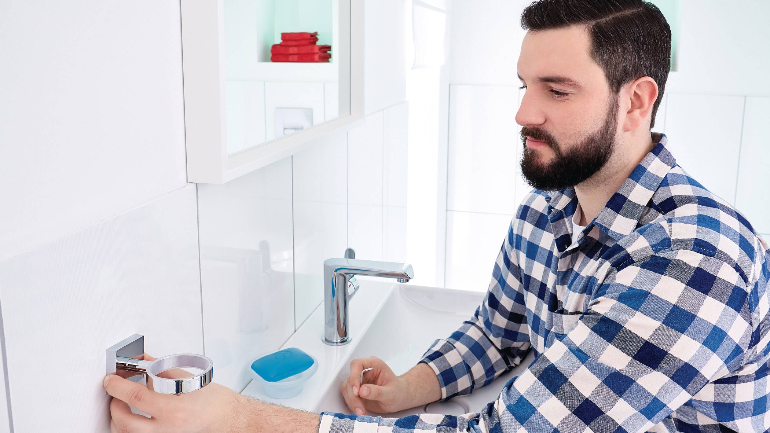 Un homme portant une chemise à carreaux tourne le robinet dans une salle de bain moderne pour se laver les mains.