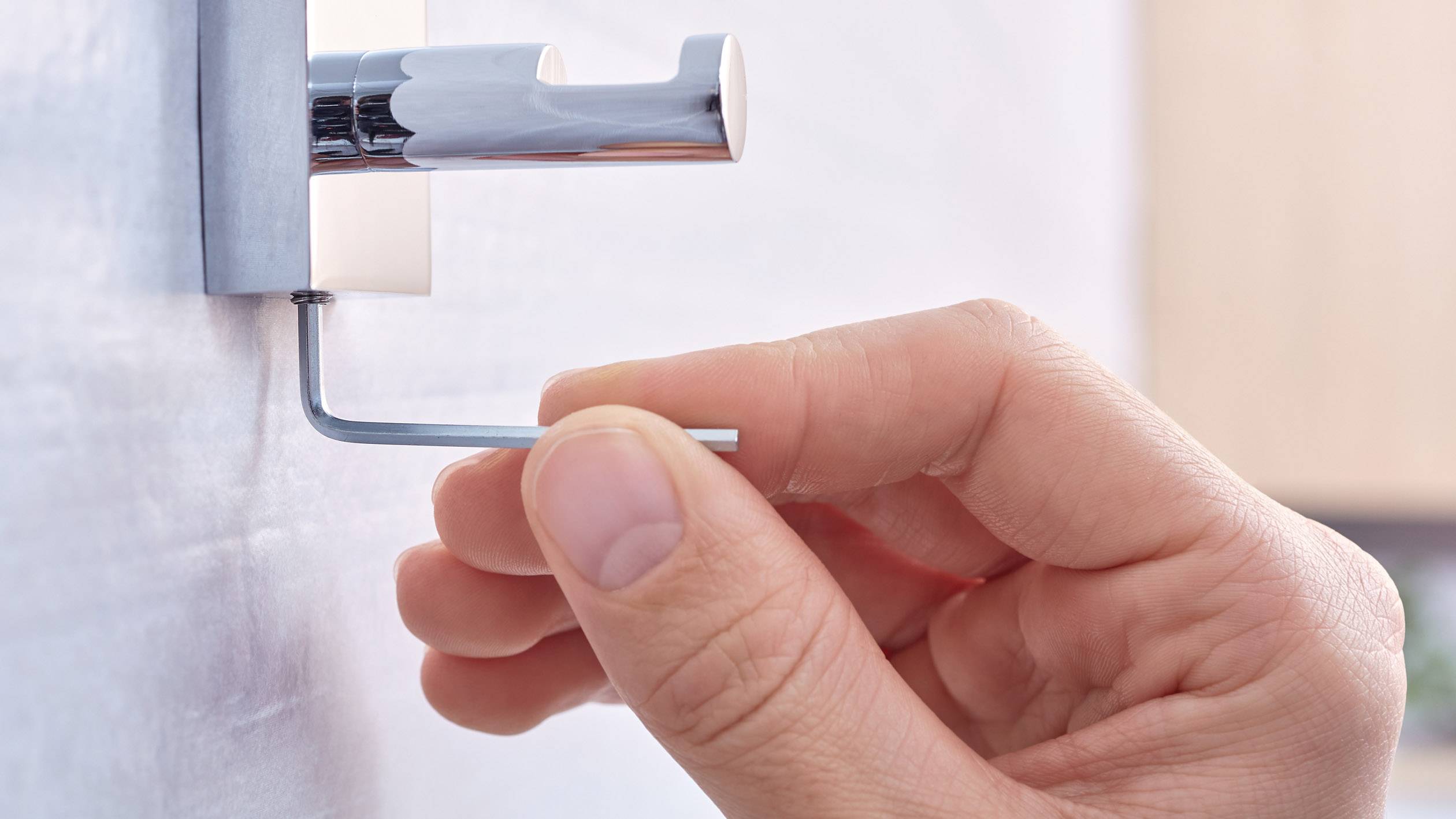 Une main utilise une clé allen pour installer un crochet mural. L'arrière-plan est flou.