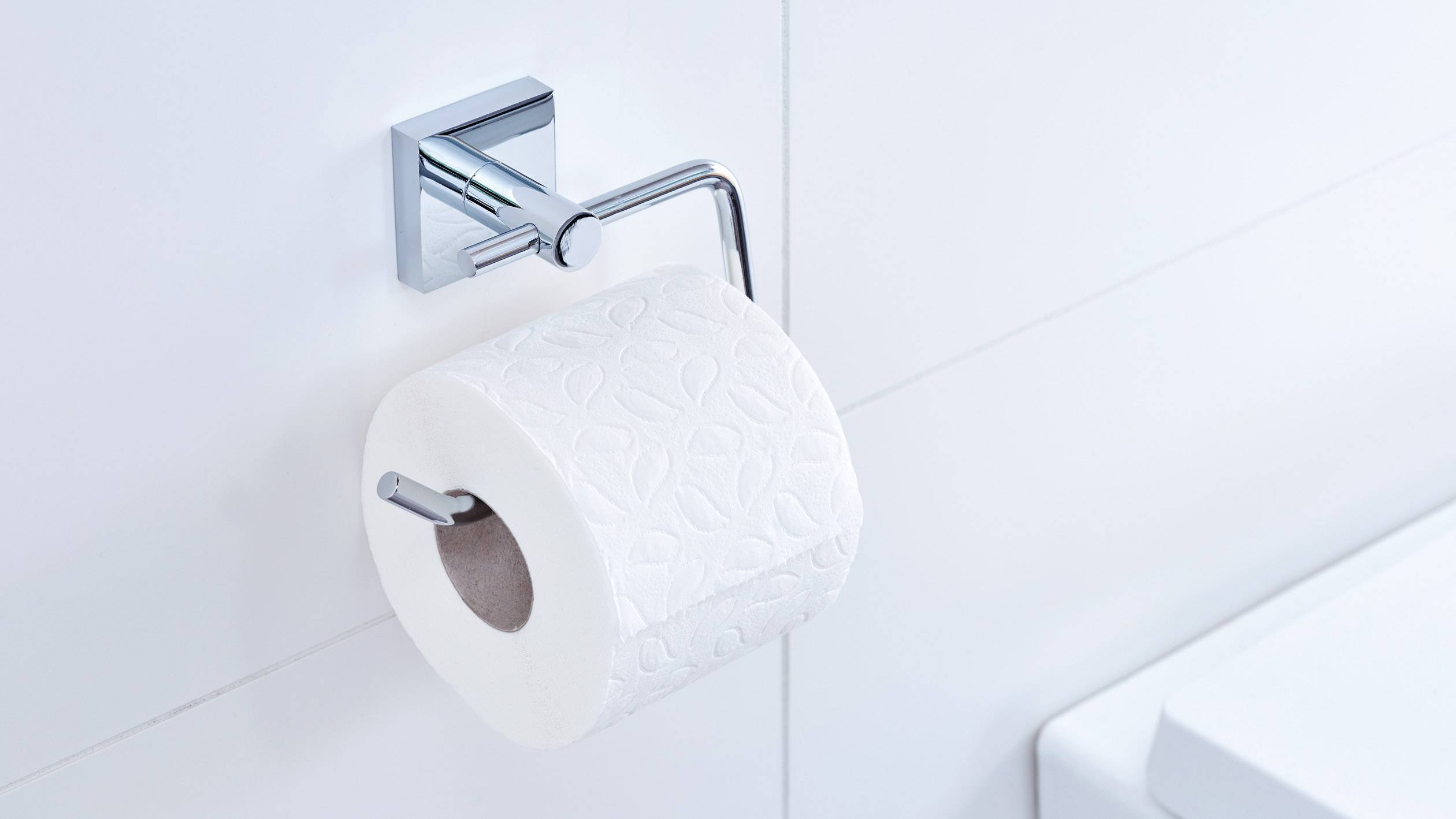 Un rouleau de papier toilette est accroché à un support métallique dans une salle de bain blanche.