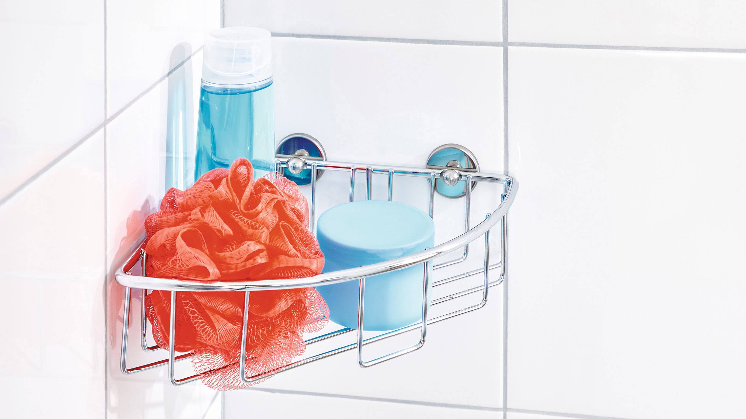 Un panier de douche sur des carreaux blancs contient une fleur de douche orange, un shampooing bleu et un pot de crème bleu.