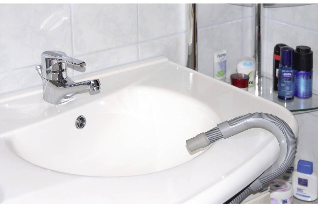 Un lavabo avec un tuyau d'aspirateur placé dans le drain. Des articles de salle de bain sont disposés autour du lavabo.