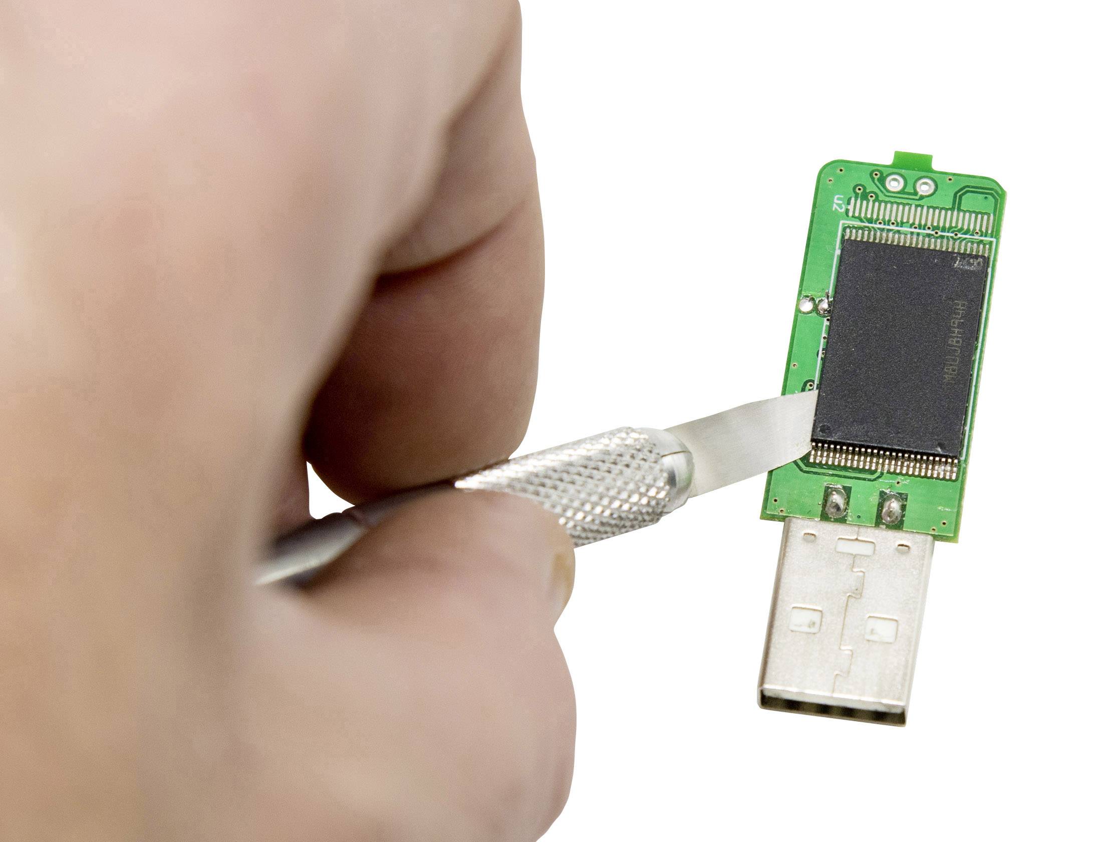 Une main tient un scalpel qui met à nu un circuit imprimé sur une clé USB.