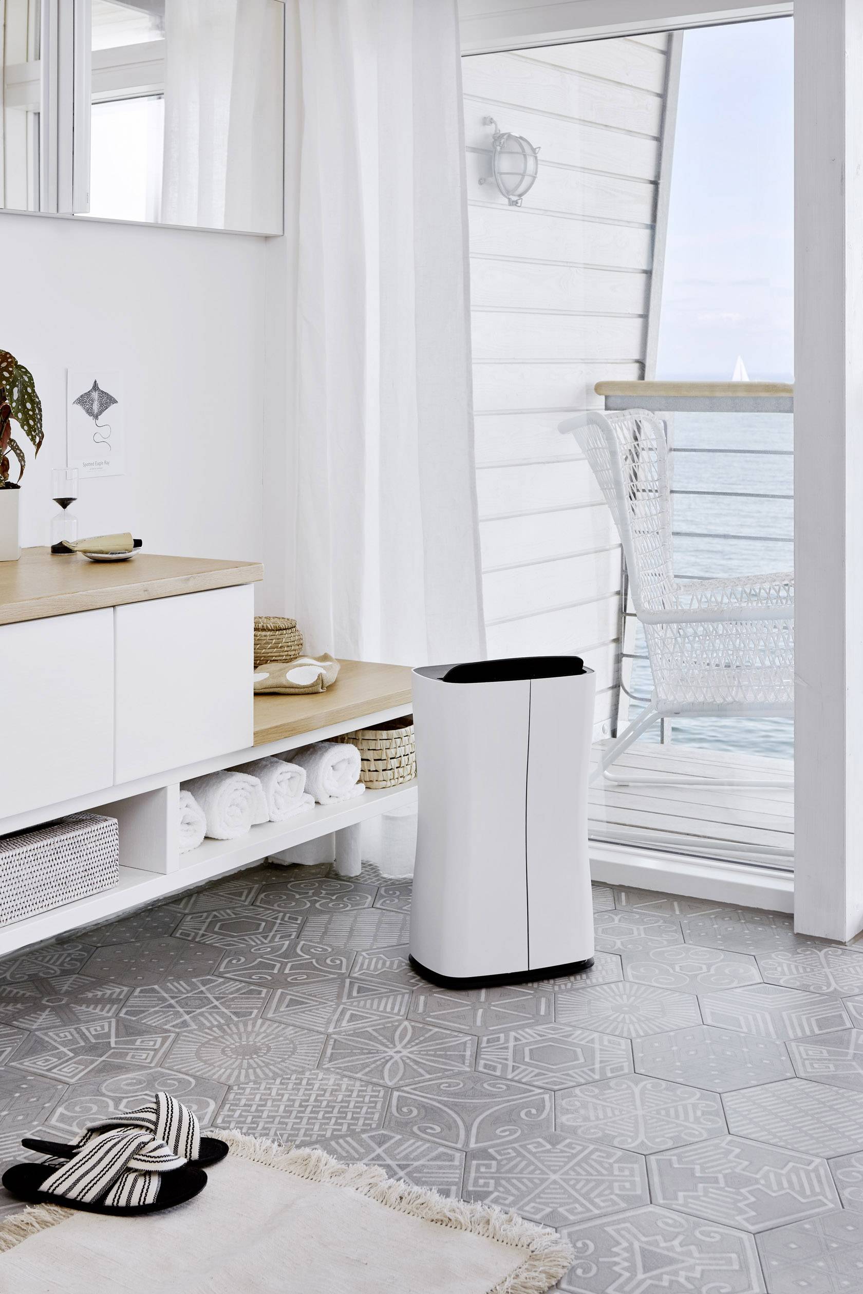 Salle de bain lumineuse avec vue sur la mer. Un purificateur d'air blanc et élégant est placé à côté d'un lavabo moderne.