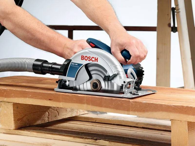 «Une personne utilisant une scie circulaire Bosch pour couper une planche en bois, démontrant une tâche de menuiserie avec précision.»