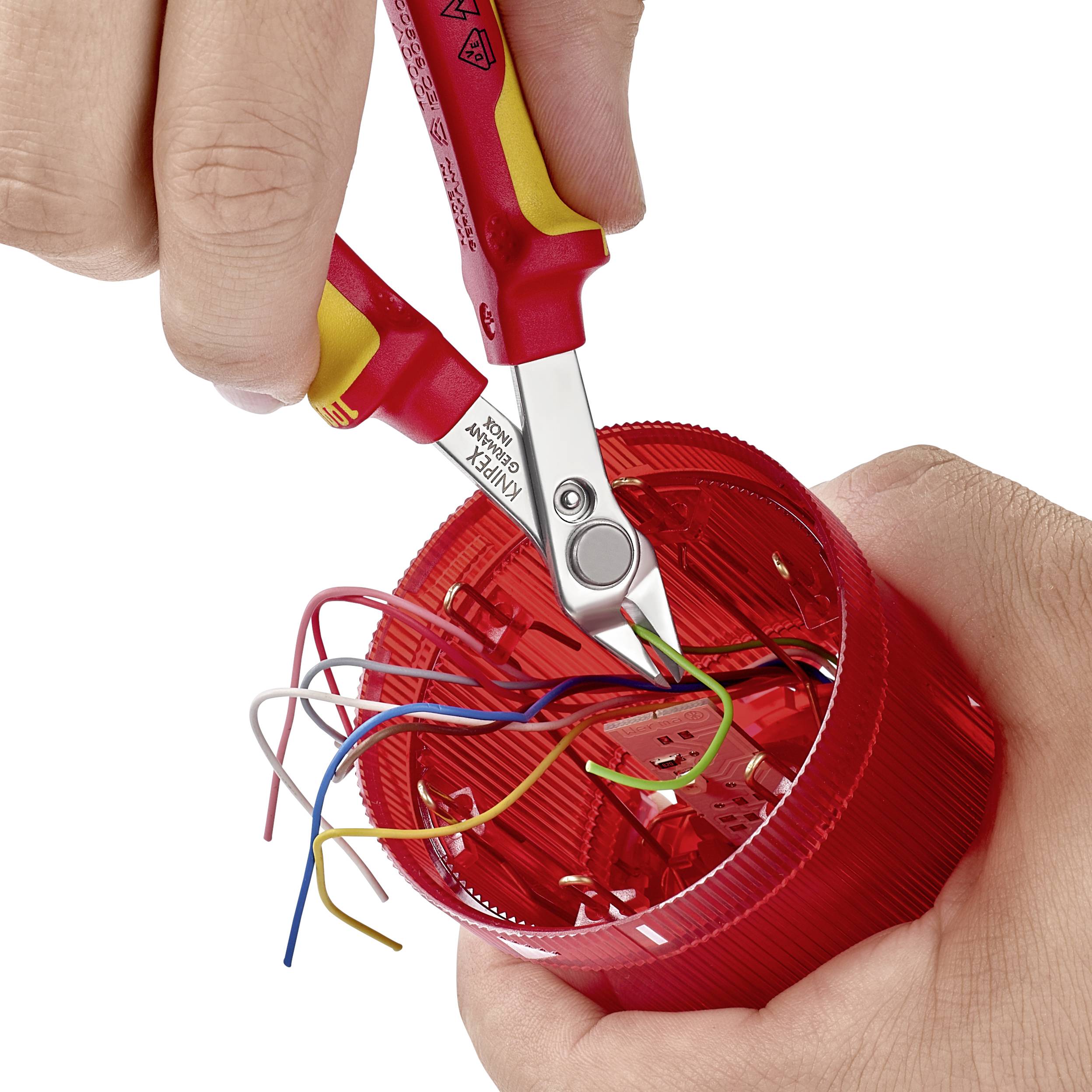Une main utilise un coupe-fil pour couper des câbles colorés dans un boîtier en plastique rouge.