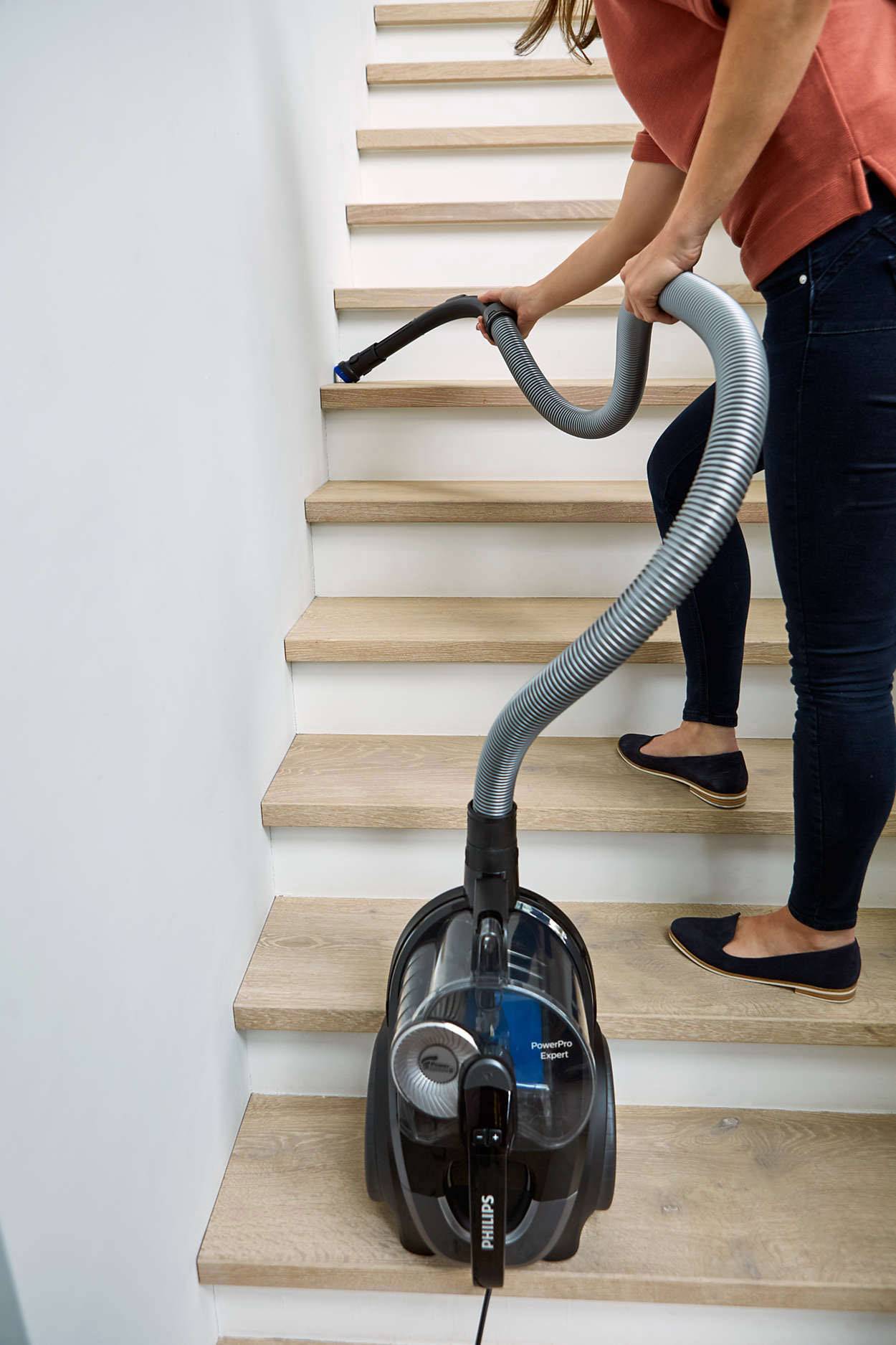 Une personne aspire les escaliers avec un aspirateur. L'aspirateur est solidement posé sur une marche.