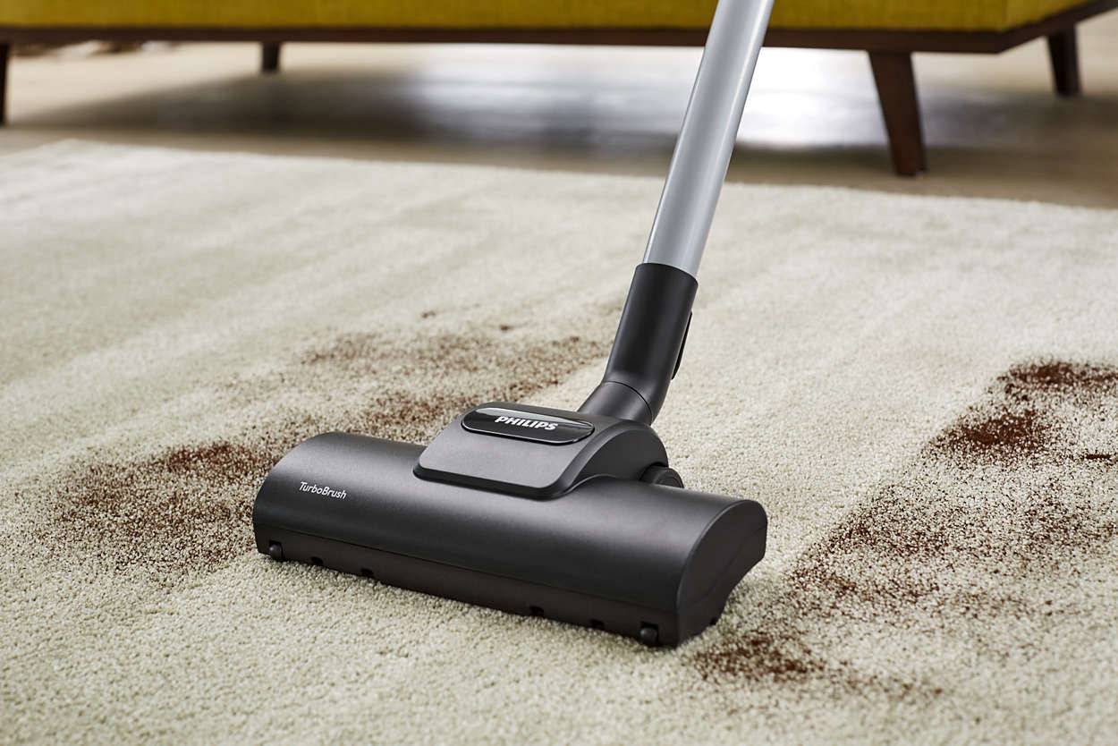 L'aspirateur aspire la saleté sur un tapis beige. Un canapé jaune est visible en arrière-plan.