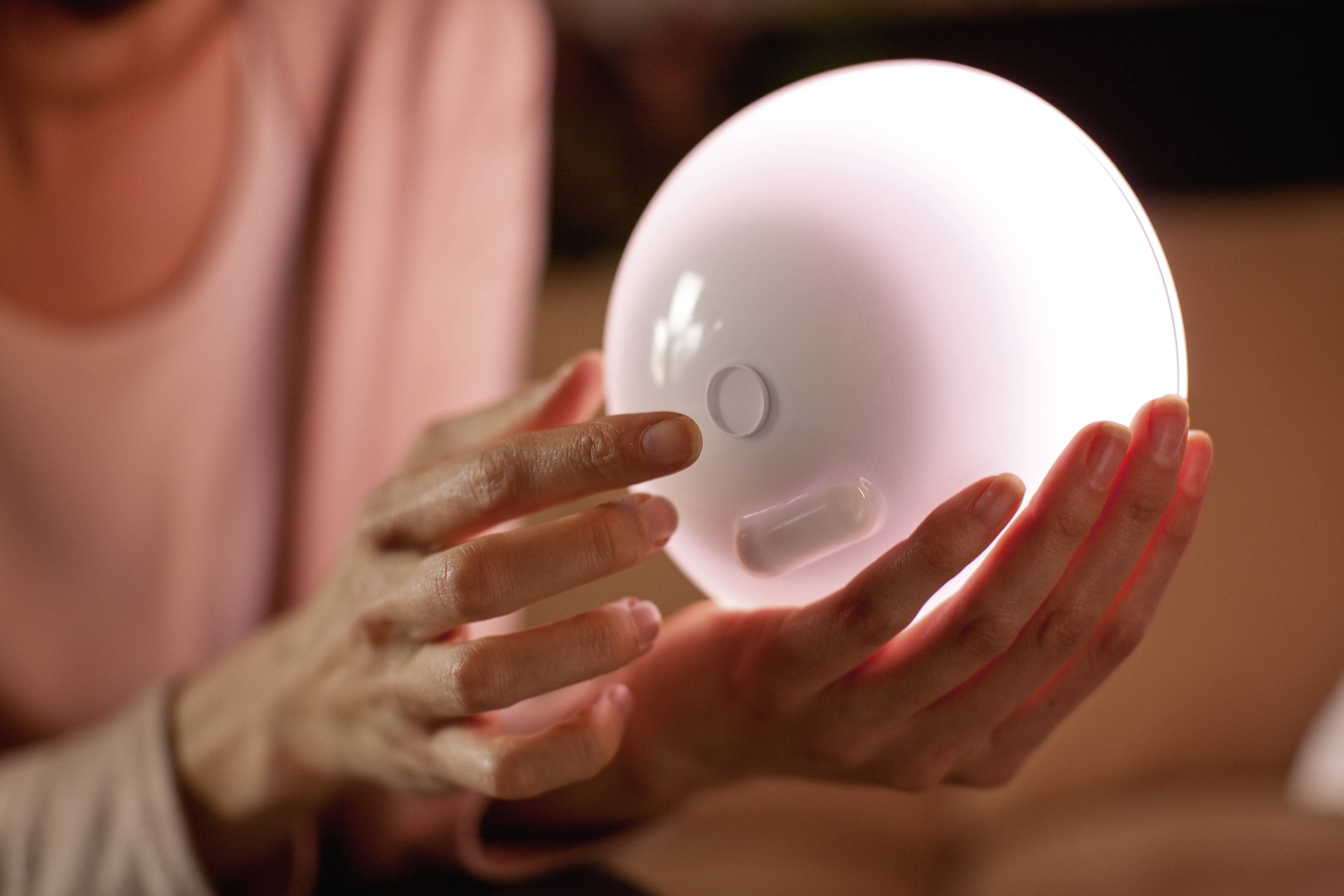 Une personne tient une lampe ronde et lumineuse dans ses mains. La lampe diffuse une lumière douce et chaleureuse qui éclaire paisiblement la pièce.