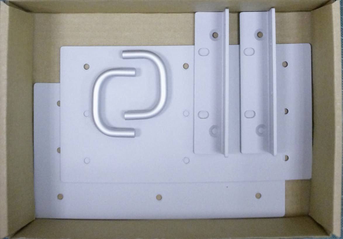 Plaques métalliques blanches et supports dans un carton. Les plaques ont des trous pour les vis. Une poignée métallique en forme de U est posée au-dessus.