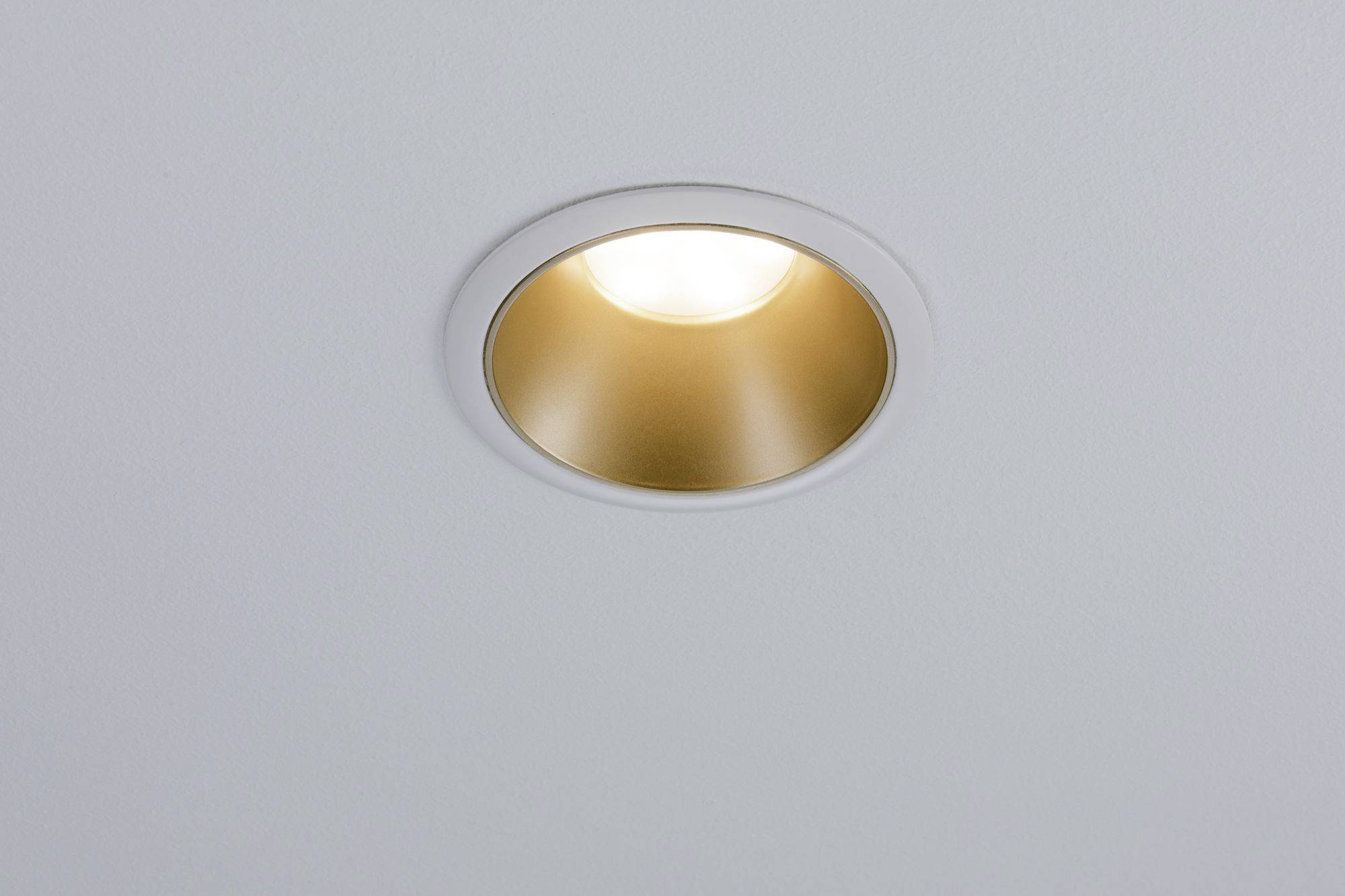 Une unique lampe dorée au plafond brille sur un fond blanc épuré.