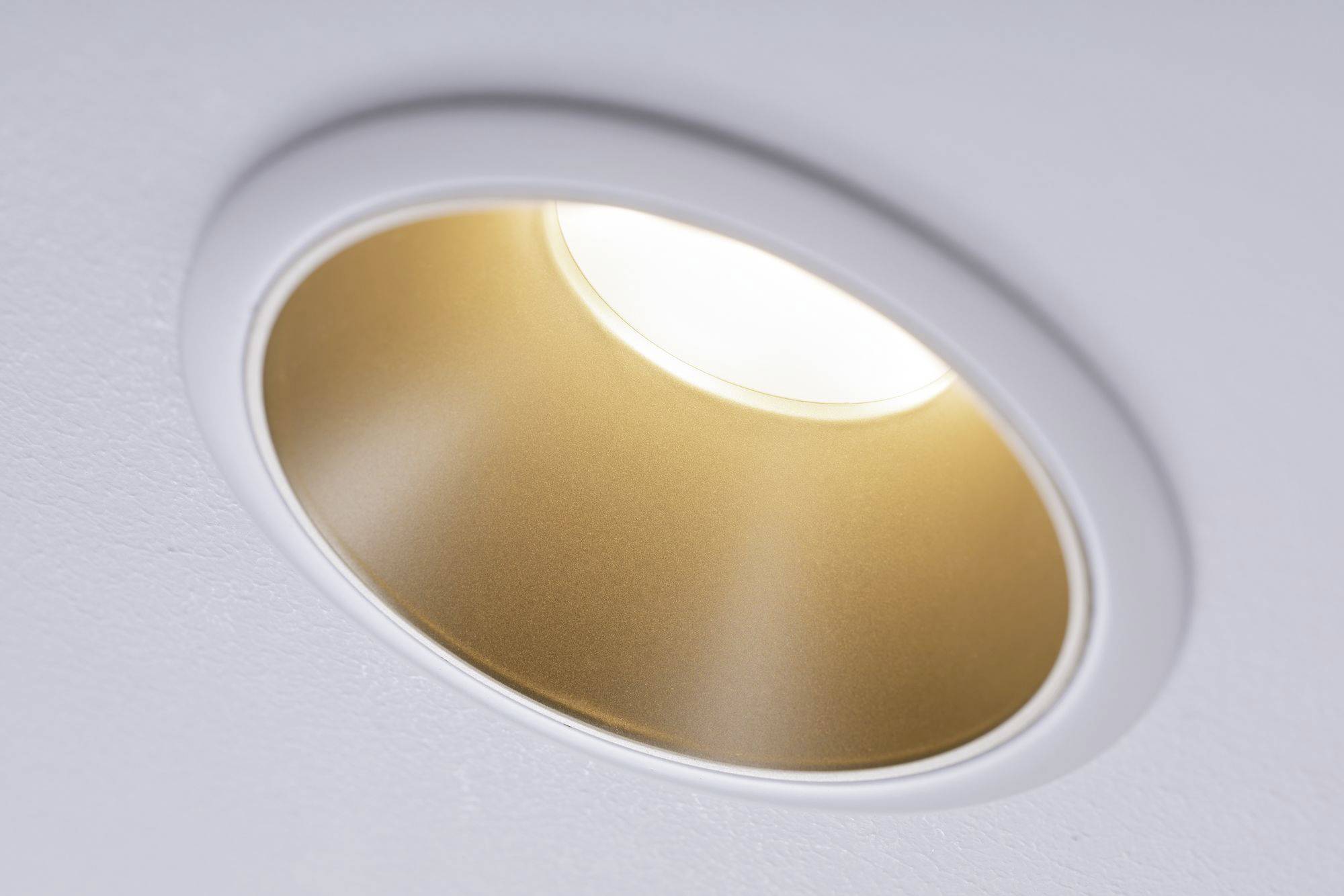 Un luminaire encastré rond au plafond brille intensément depuis le haut. Le support est blanc avec un bord intérieur doré, assurant un éclairage uniforme.