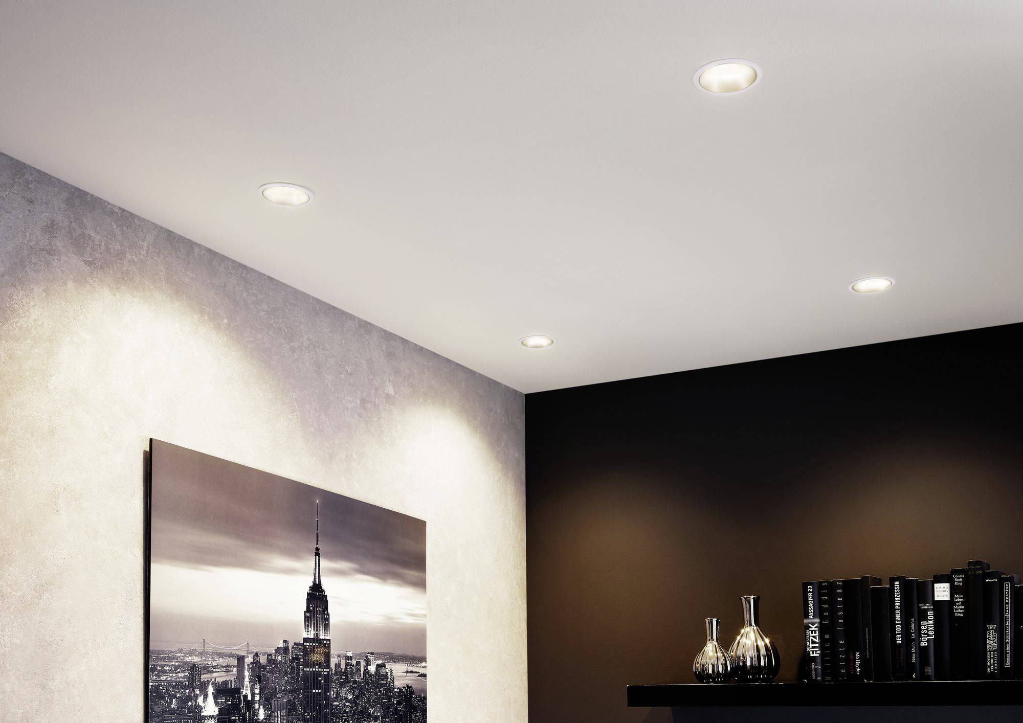 Chambre avec un éclairage moderne, quatre spots encastrés au plafond, photo d'un paysage urbain sur le mur et une bibliothèque à droite.