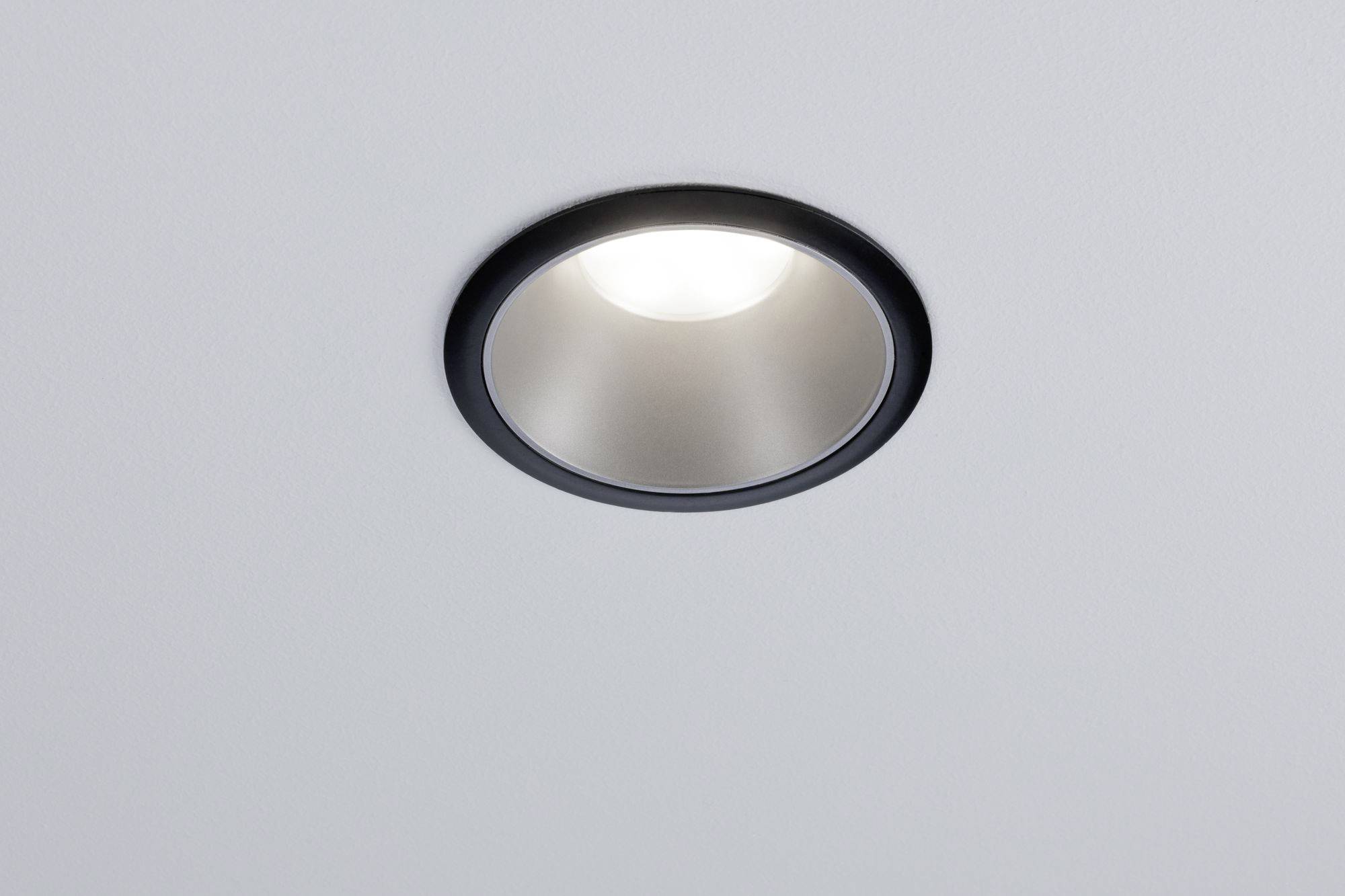 Plafonnier rond et argenté avec bordure noire, illuminant brillamment un plafond blanc.
