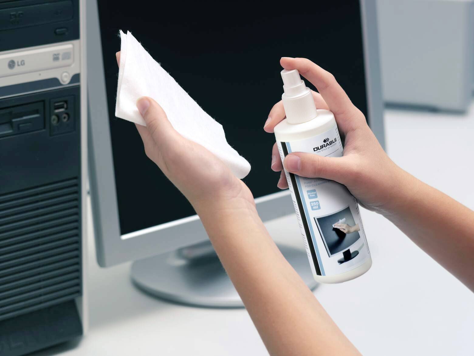 Personne nettoyant un écran d'ordinateur avec une solution de nettoyage et un chiffon. L'ordinateur est éteint et l'environnement est un bureau.