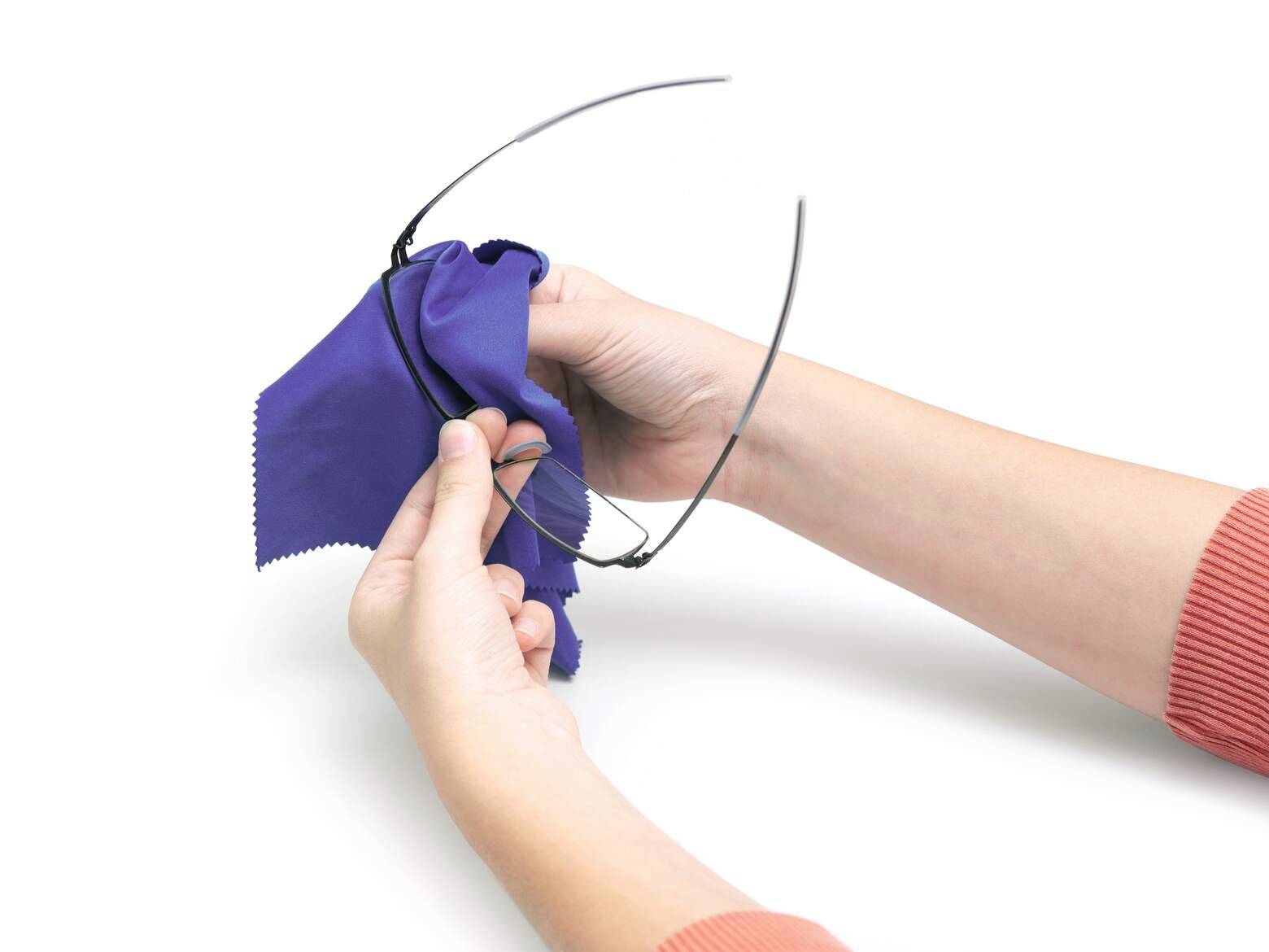 Personne nettoyant des lunettes avec un chiffon en microfibre bleu sur un fond blanc.