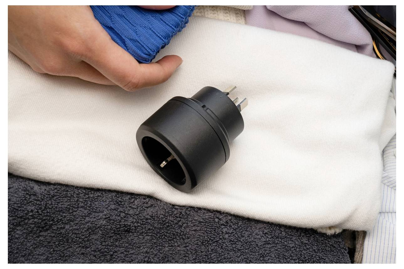 Une main dans un plâtre bleu repose à côté d'un adaptateur de prise électrique noir sur une serviette blanche, suggérant des soins ou une récupération suite à une blessure.