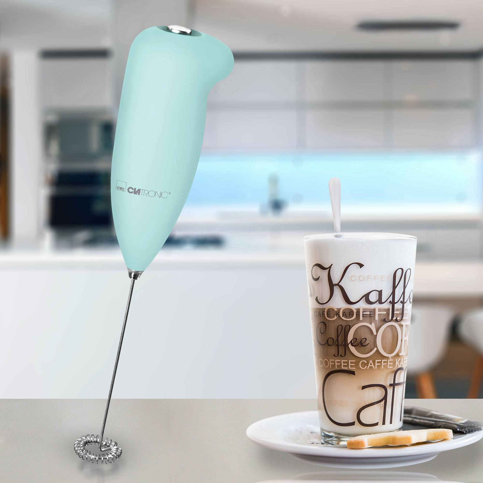 Un mousseur à lait à côté d'un verre de café dans une cuisine moderne. Le mousseur est de couleur turquoise et se tient debout.