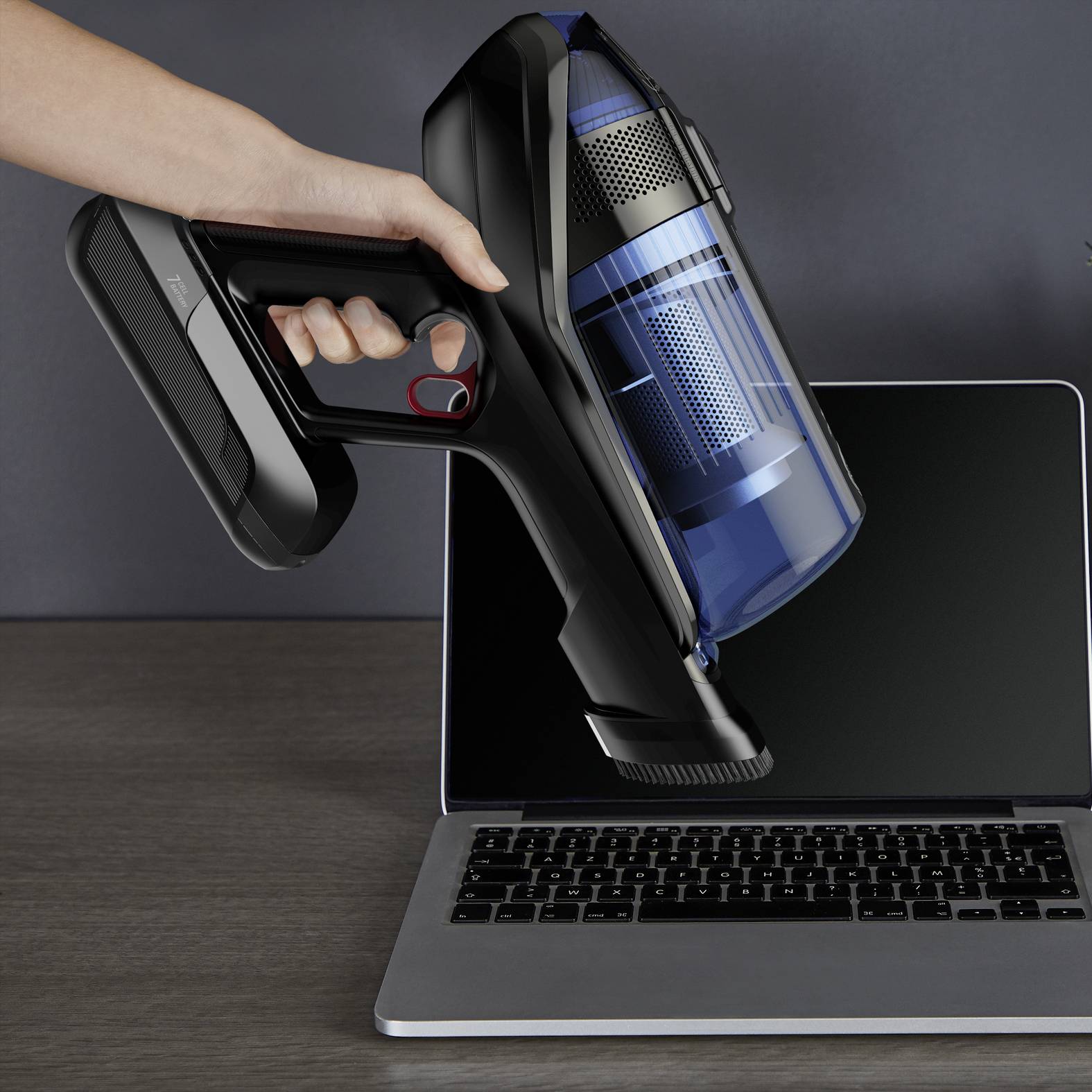 Une main tient un aspirateur au-dessus d'un clavier d'ordinateur portable pour enlever la saleté.