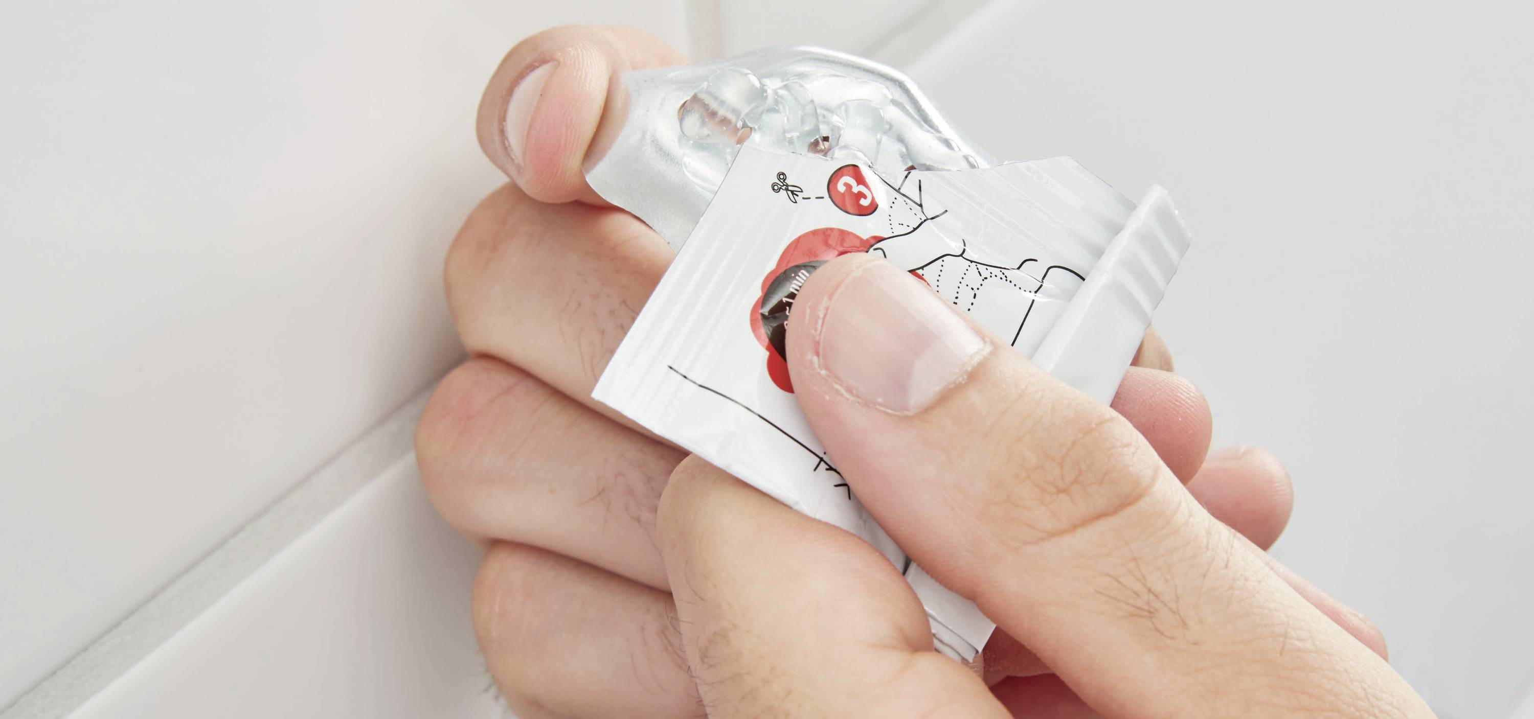 Des mains pressent un tube de dentifrice contre le mur pour en extraire les derniers restes.