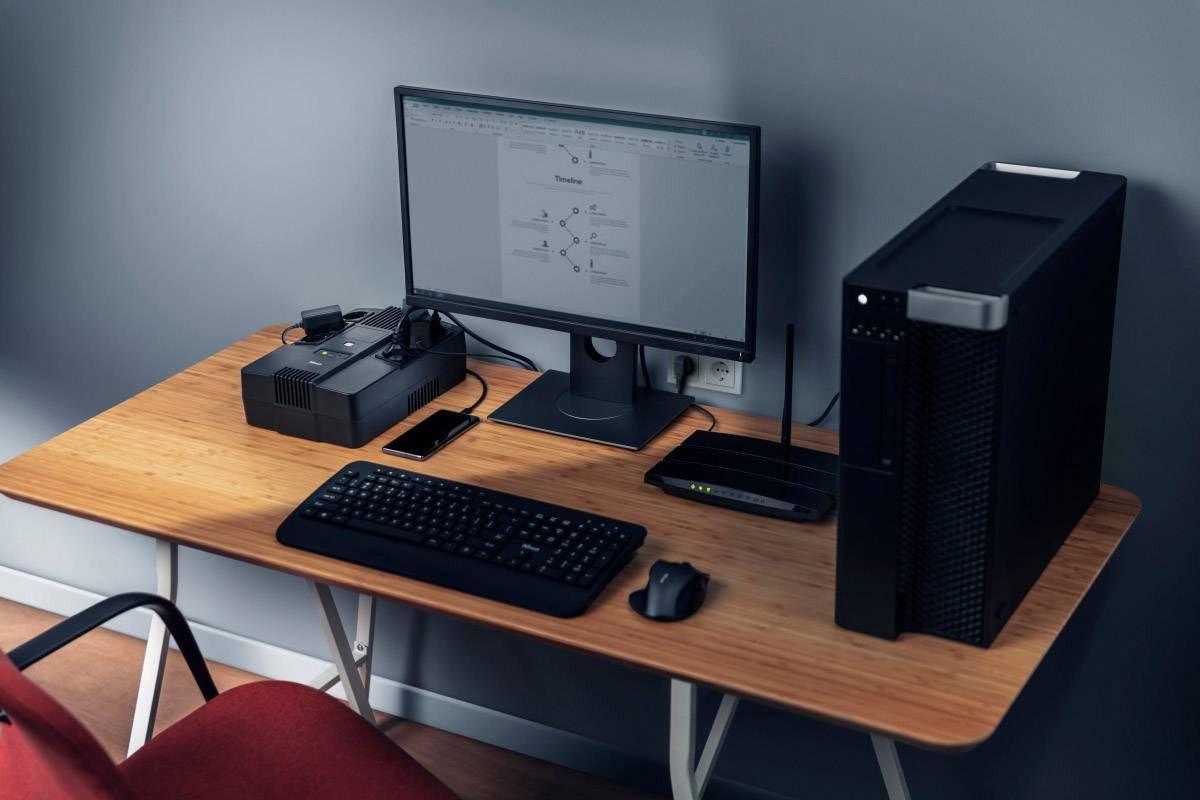 Un bureau avec un ordinateur, un écran, un clavier, une souris, un smartphone et un routeur. L'écran affiche un document.