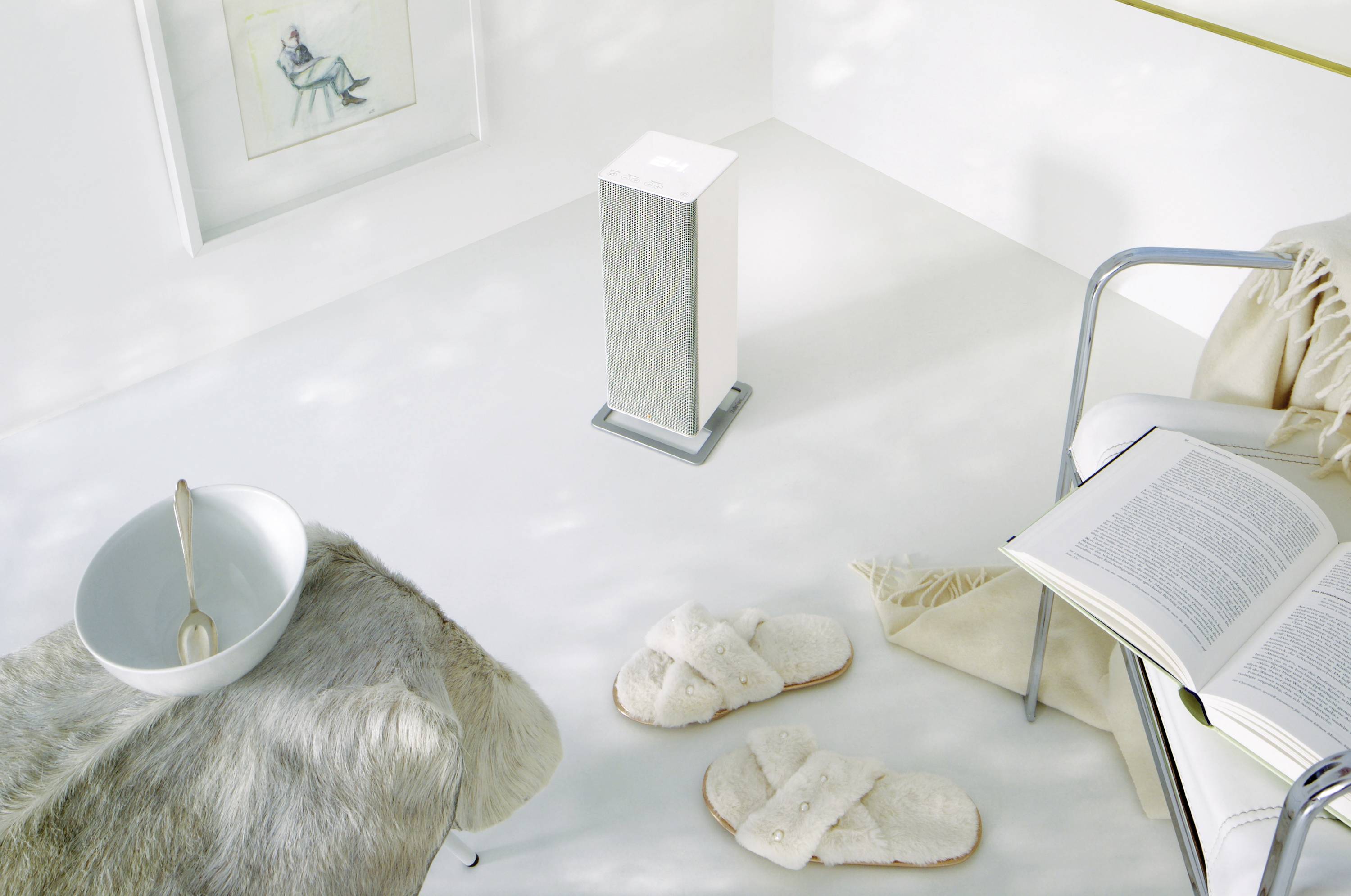 Un espace douillettement aménagé avec un haut-parleur blanc au centre, un livre posé sur un fauteuil et des pantoufles moelleuses.