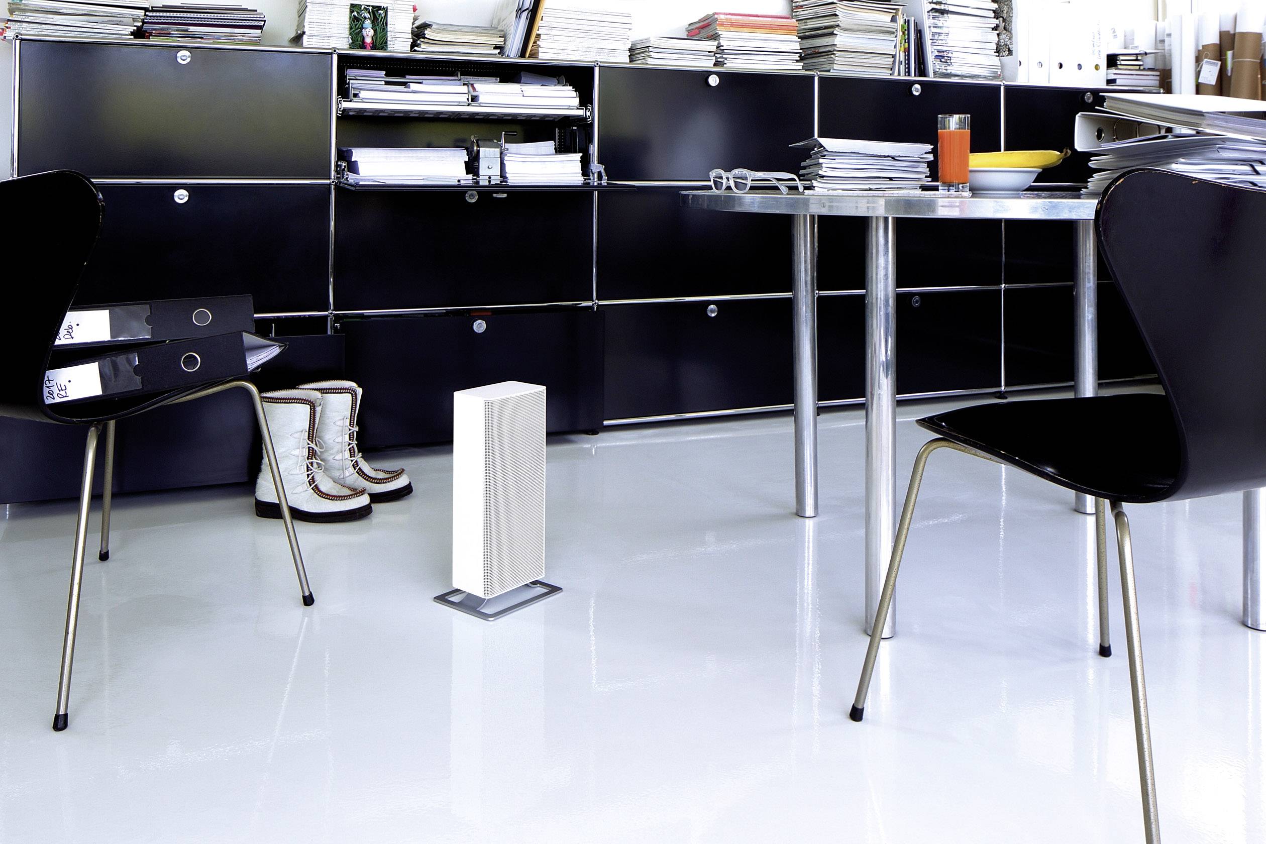 Un bureau moderne avec des armoires noires, une table, deux chaises et un purificateur d'air. Un verre de boisson à l'orange est posé sur la table.