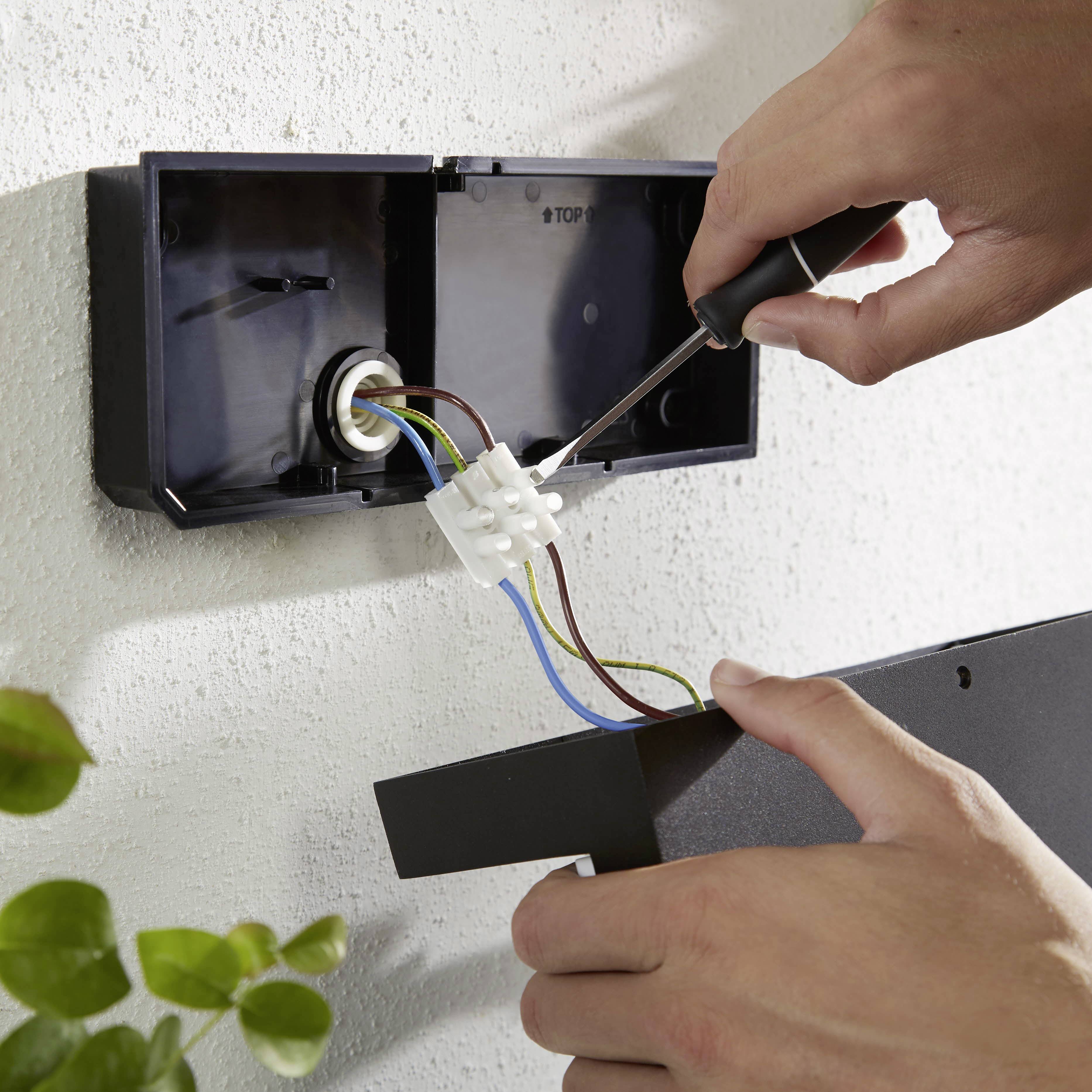 Une personne installe une prise électrique en connectant des câbles avec un tournevis dans un boîtier de raccordement.