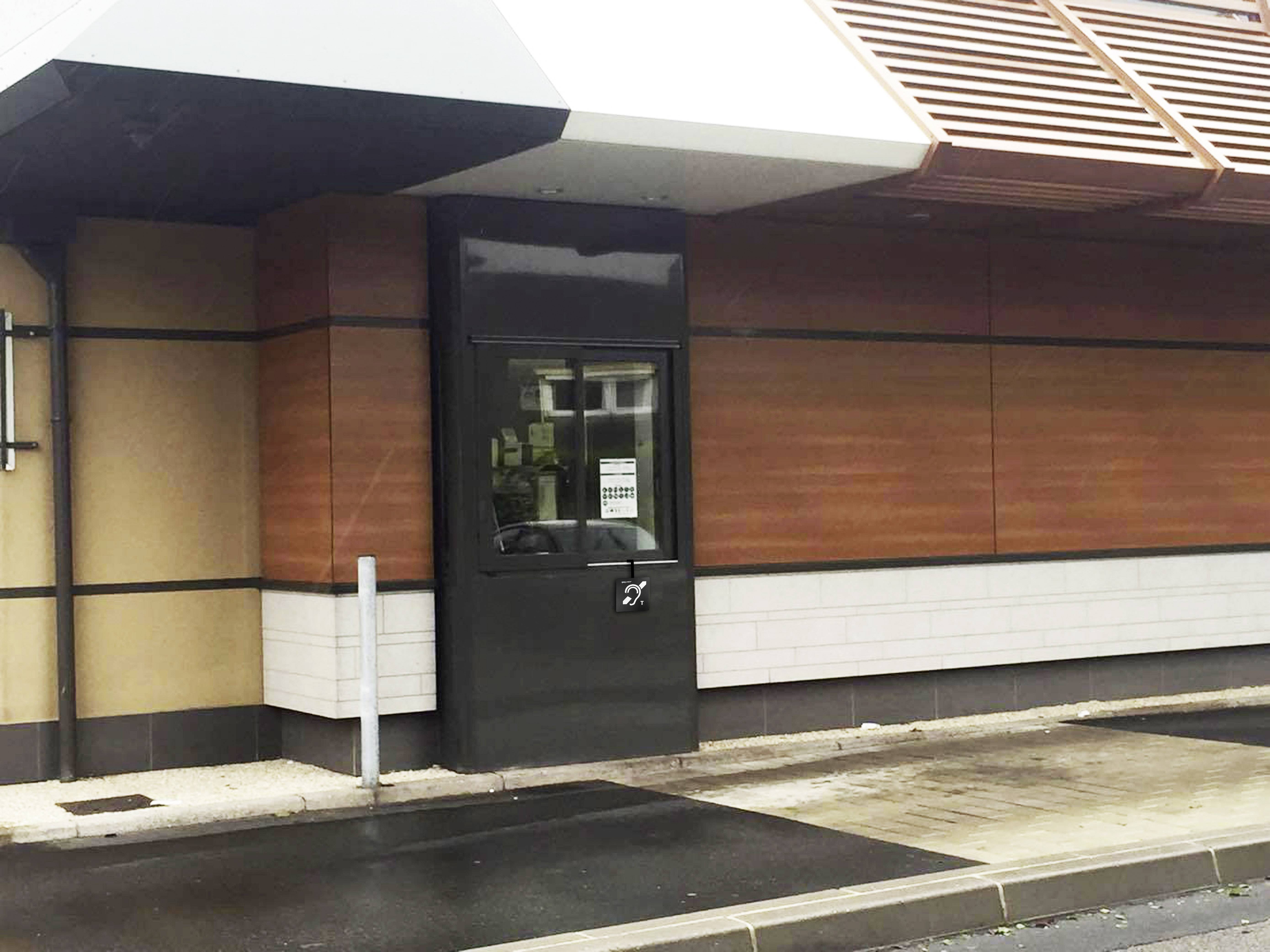 Un restaurant de restauration rapide avec un guichet de service au volant, vitres teintées dans un habillage en bois. Le temps est nuageux, le trottoir est mouillé.