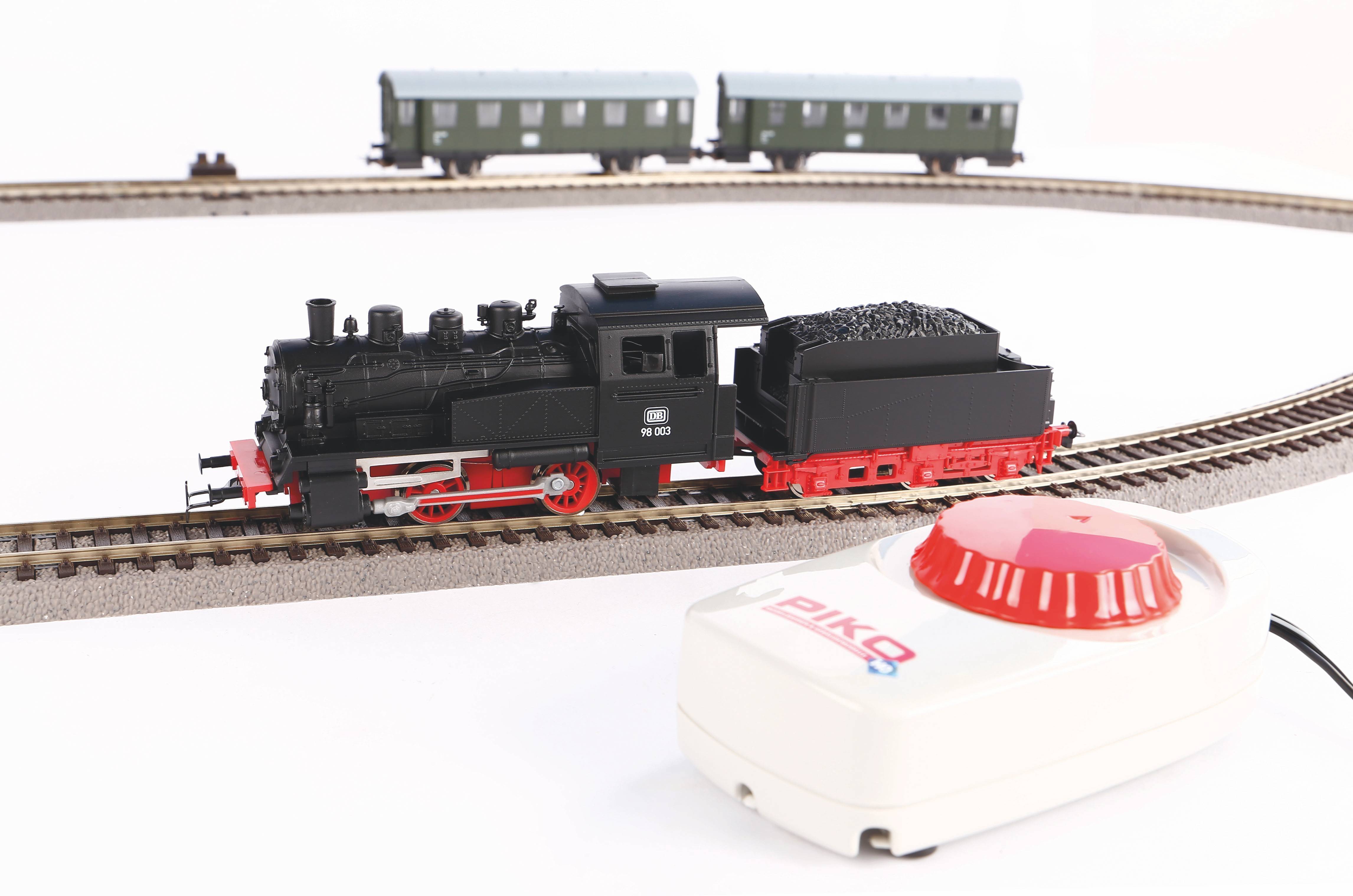 Un train miniature sur un rail, avec une locomotive noire et deux wagons verts en arrière-plan, à côté d'une unité de commande.
