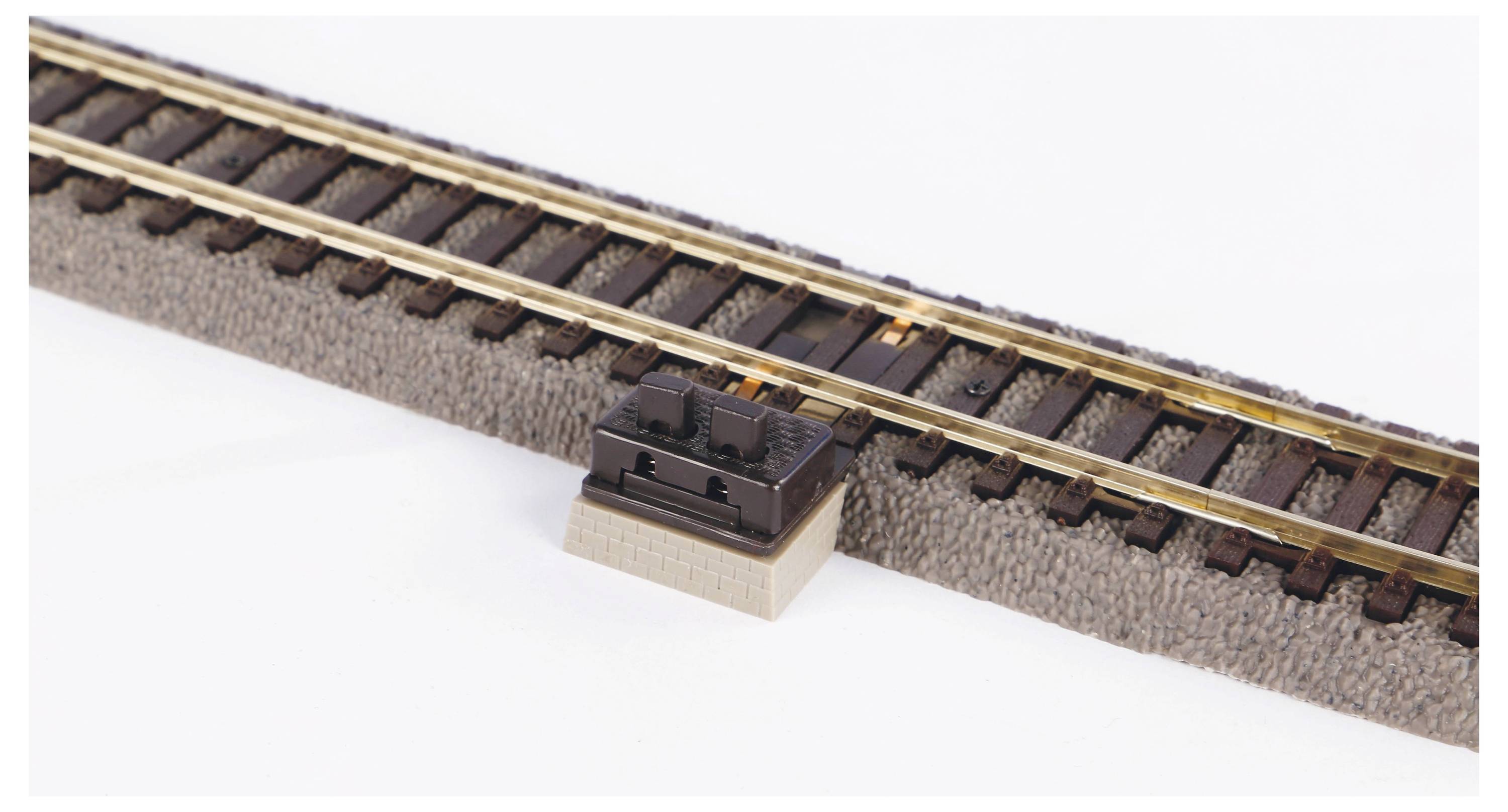 Un morceau de voie de chemin de fer miniature avec deux rails, monté sur un socle rectangulaire, beige et marron, sur un fond clair.