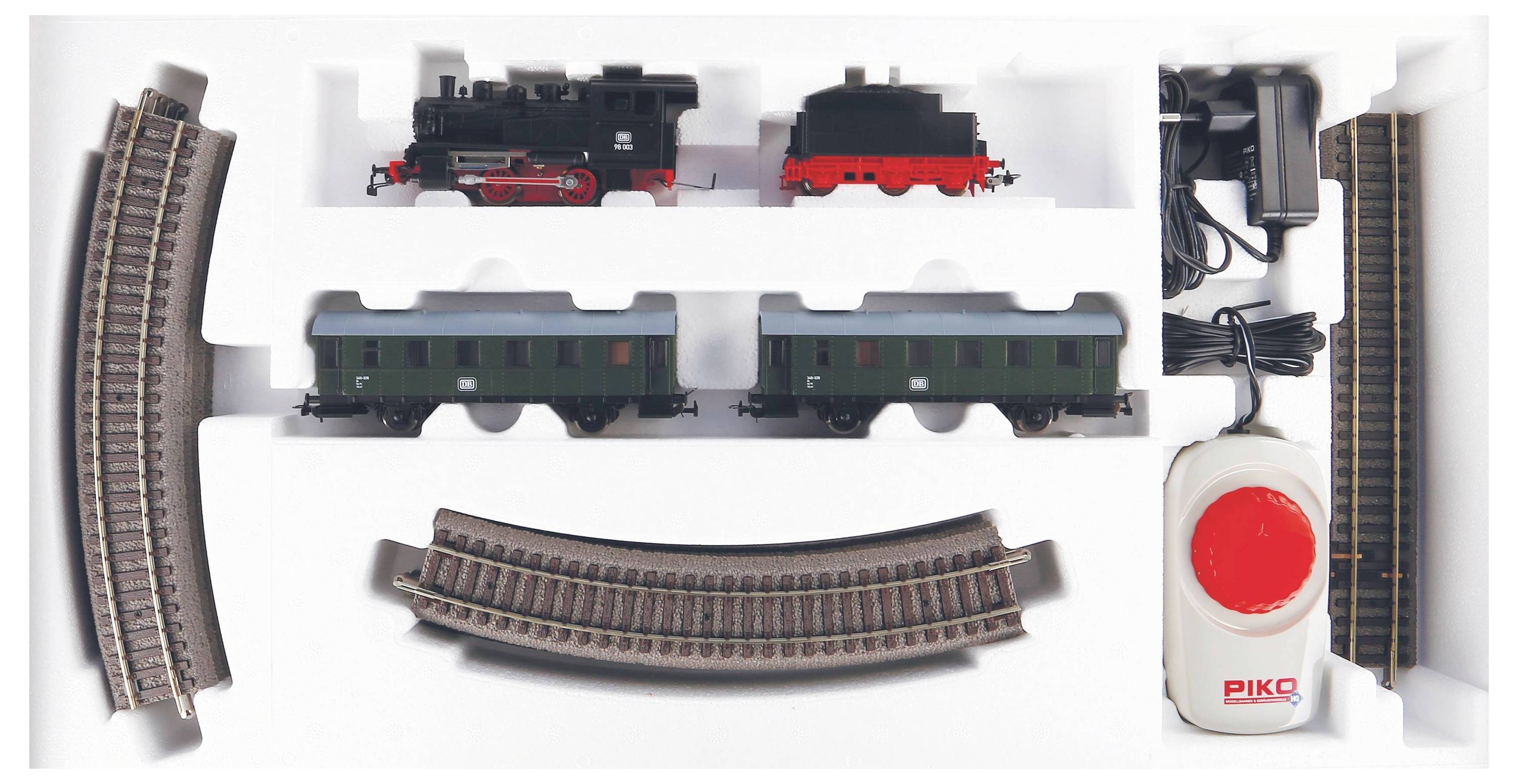 Ensemble de train miniature comprenant une locomotive à vapeur, deux wagons, des rails courbes et droits, ainsi qu'un contrôleur, le tout présenté dans une mousse blanche.