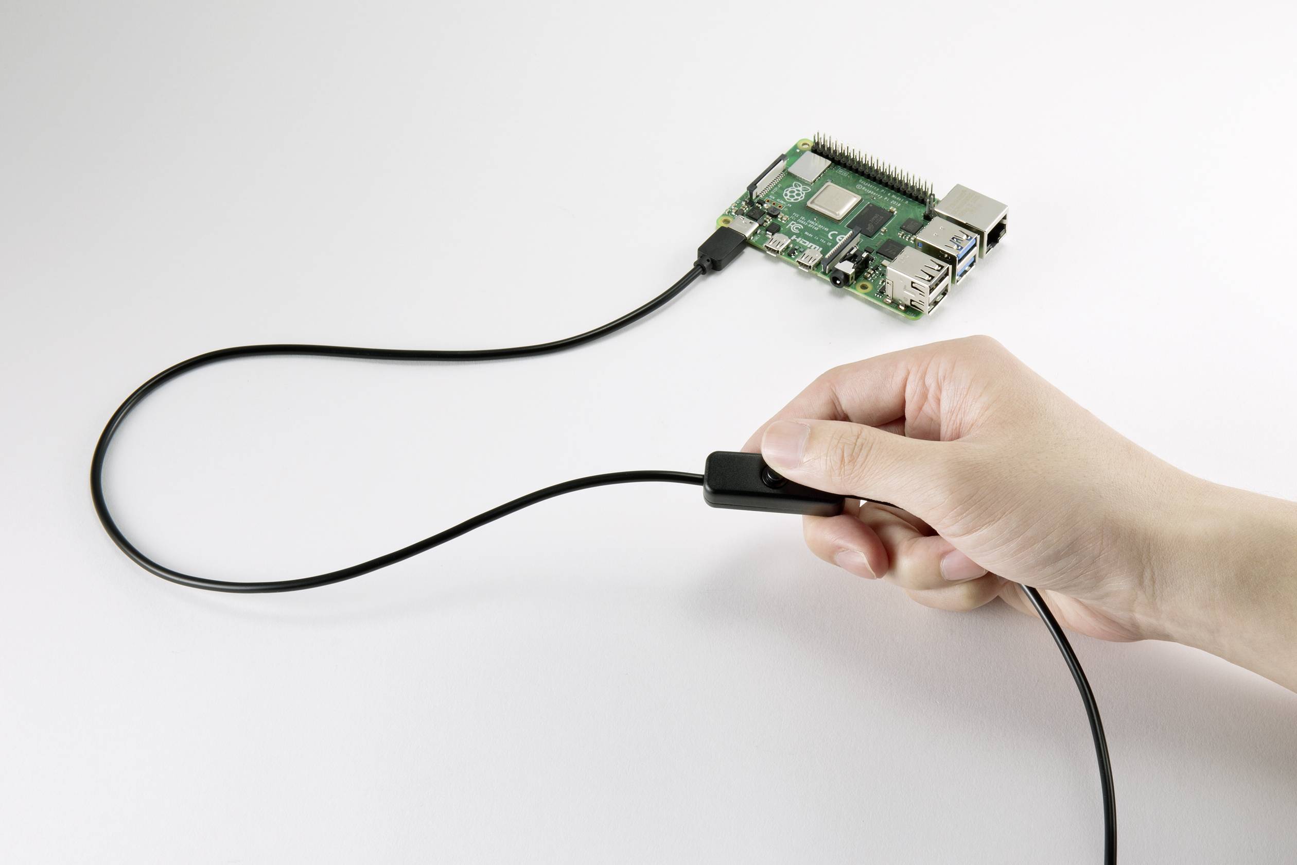 Une main tient un câble qui est connecté à un Raspberry Pi. Le Raspberry Pi est posé sur une table et est relié par le câble.