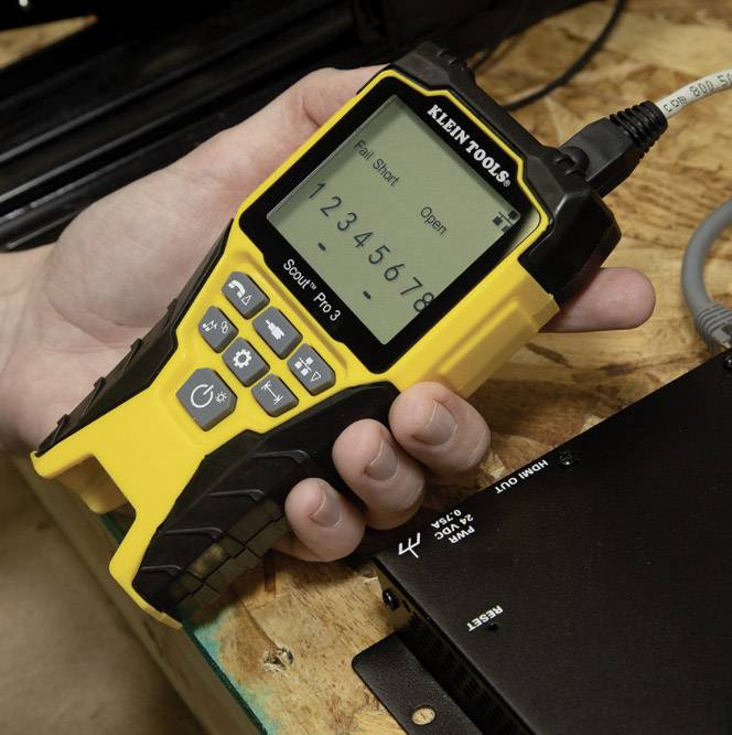 Une personne tient un appareil de test de câbles avec un boîtier jaune. L'écran de l'appareil affiche 'Pass 1 2 3 4 5 6 7 8'.