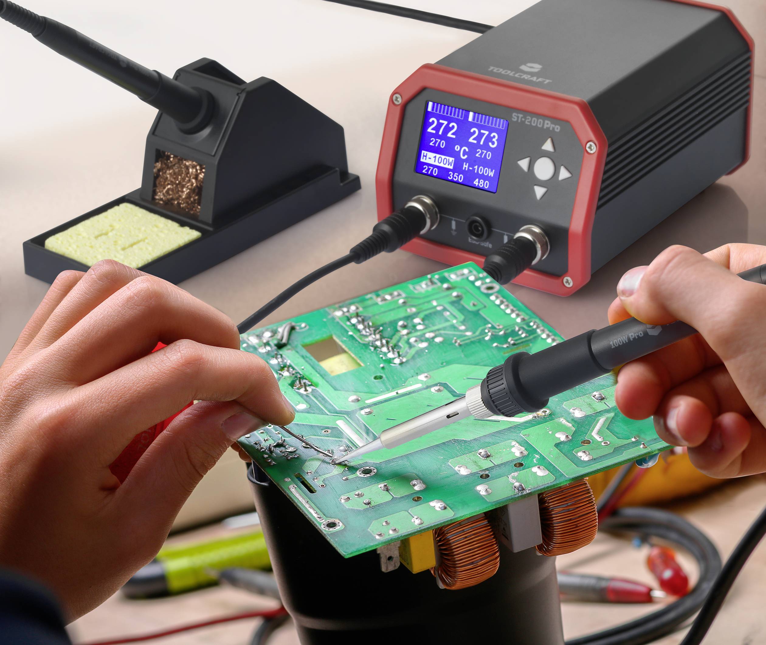 Deux mains tiennent un fer à souder et une carte de circuit imprimé ; en arrière-plan, un support de fer à souder et un affichage de température à 272°C et 273°C.