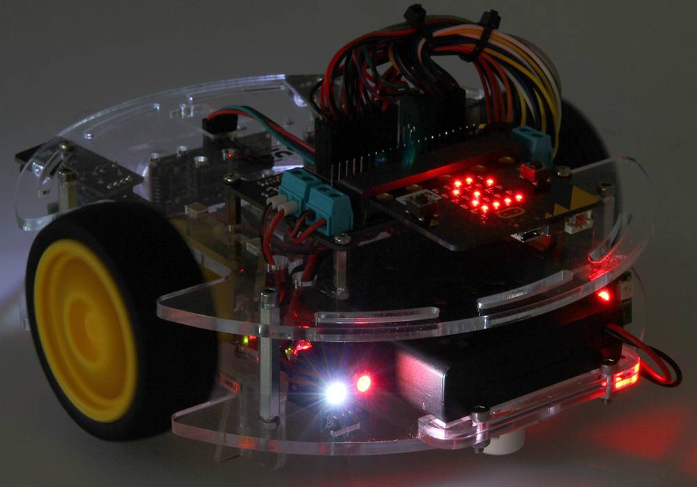 Un petit robot programmable avec des roues jaunes et des voyants LED lumineux sur une plateforme transparente.