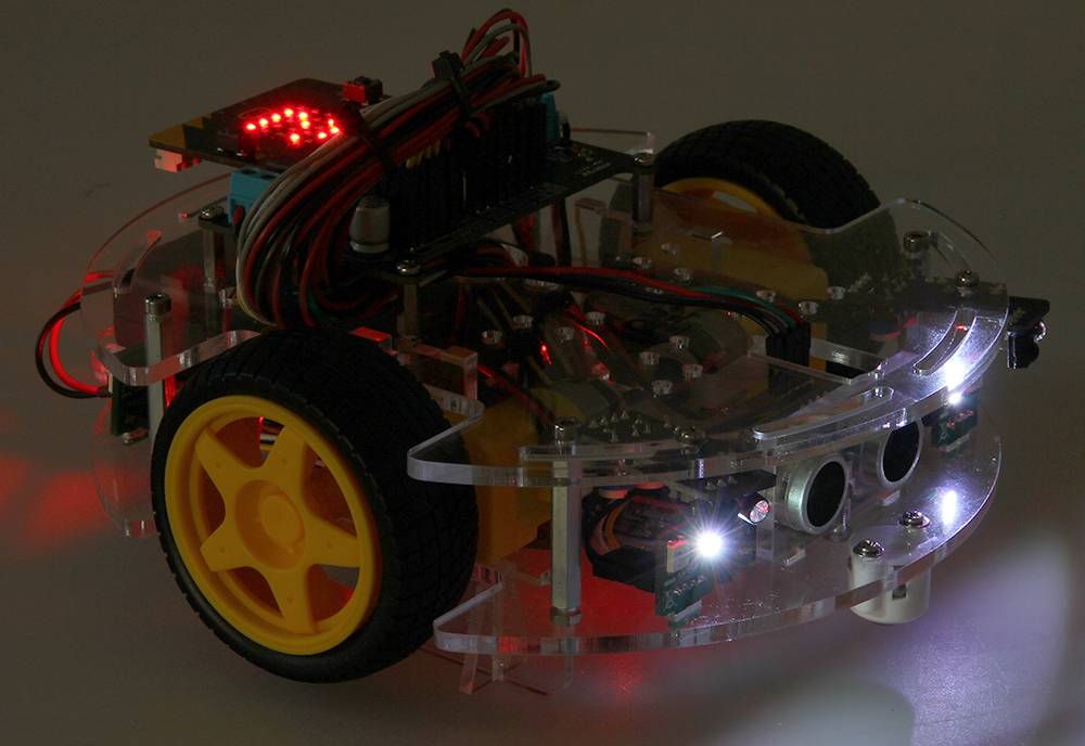 Un petit robot transparent sur roues, avec des pneus jaunes, des circuits électroniques apparents et des lumières LED brillantes.