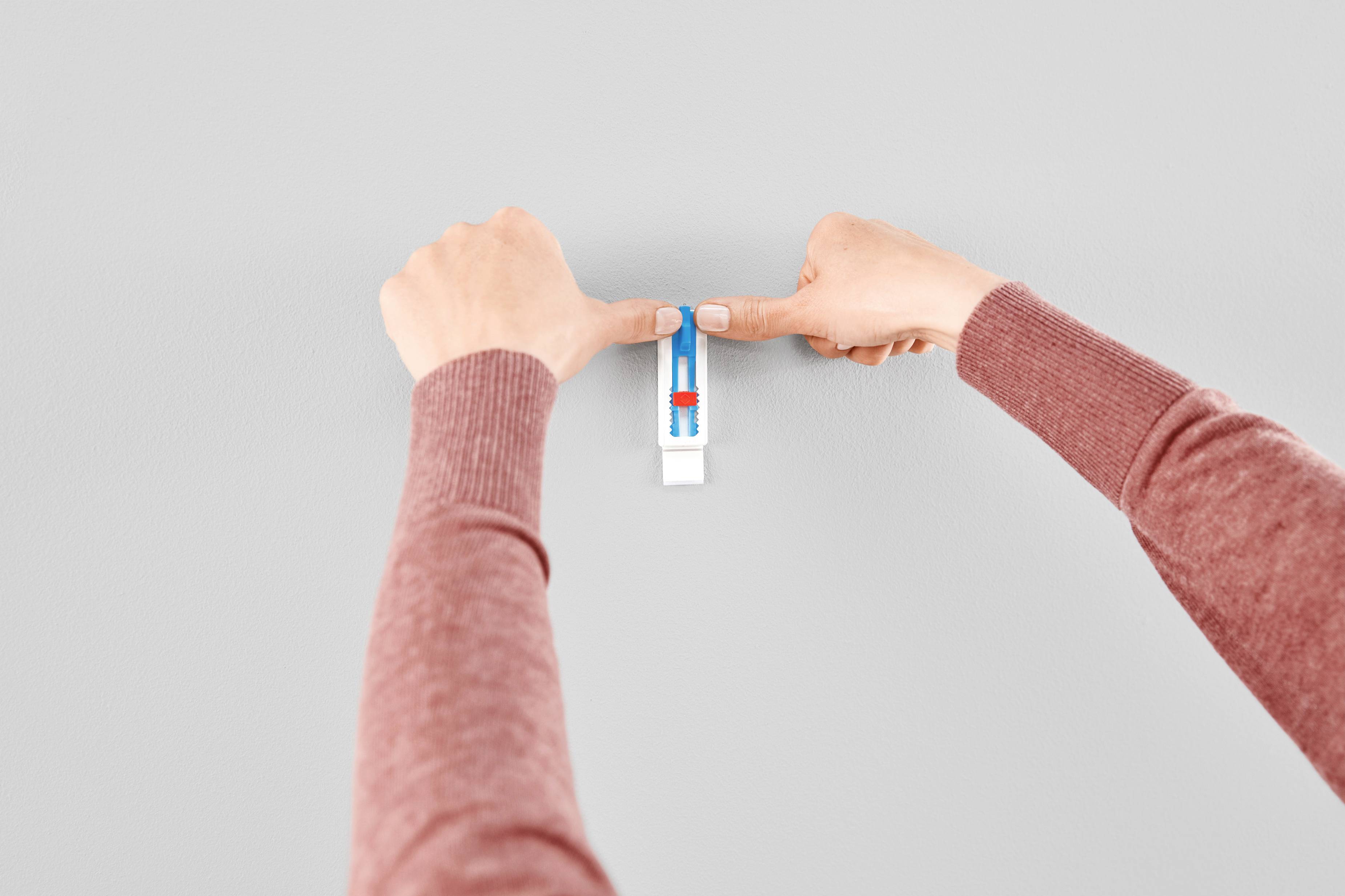 Deux mains fixent un niveau à bulle rectangulaire sur un mur gris.