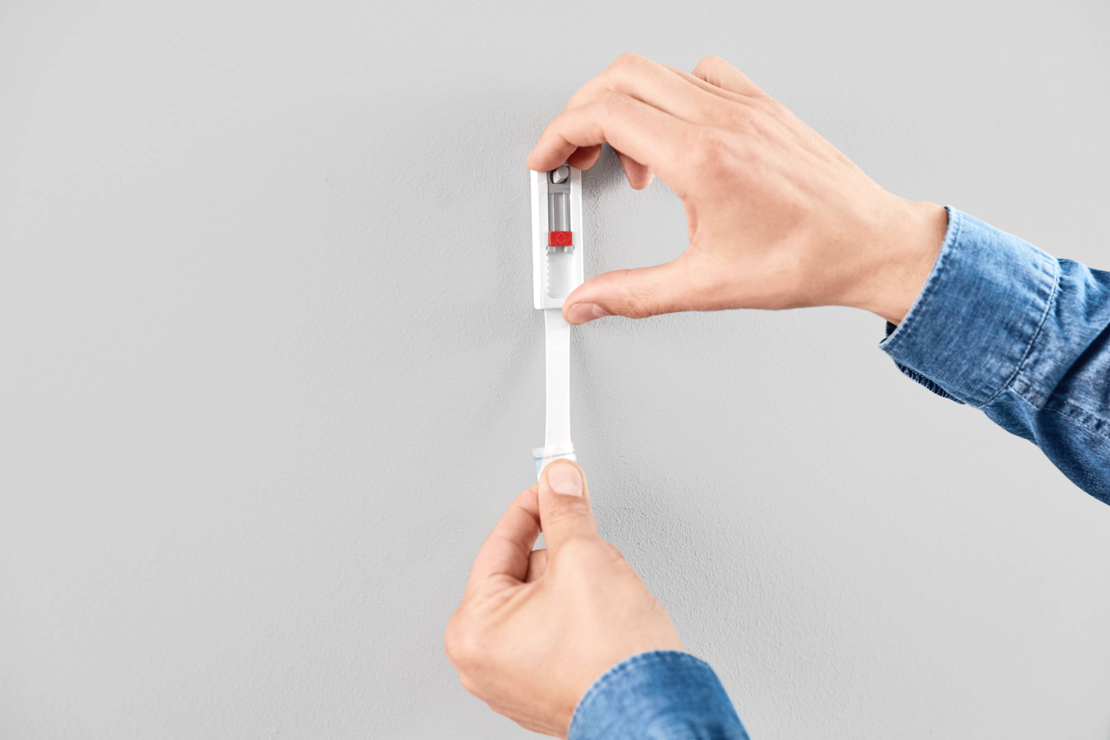 Deux mains tenant un niveau à bulle contre un mur gris clair pour vérifier l'alignement horizontal.