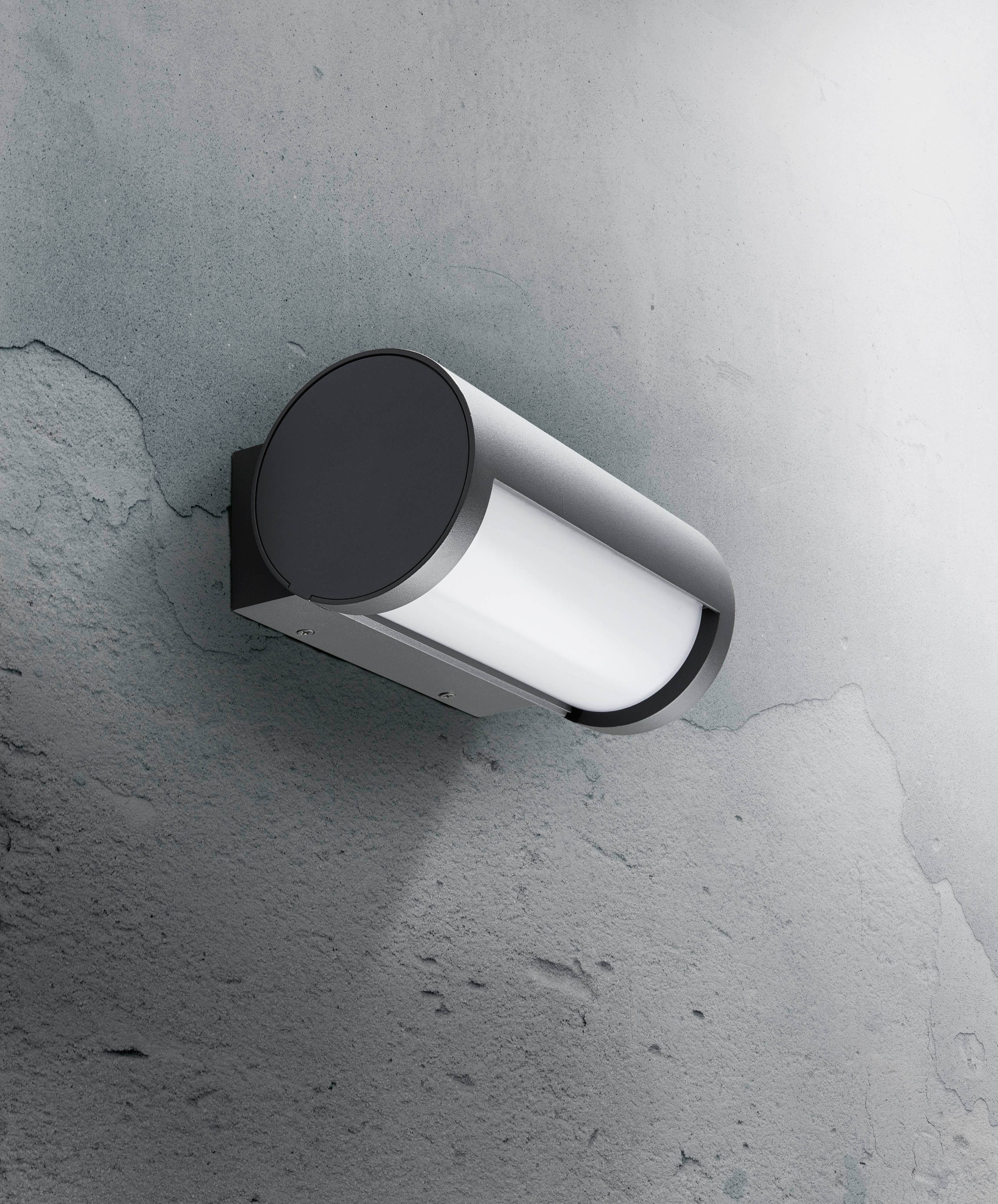 Un luminaire cylindrique moderne fixé sur un mur texturé, dirigeant sa lumière vers le bas et créant un effet lumineux doux.