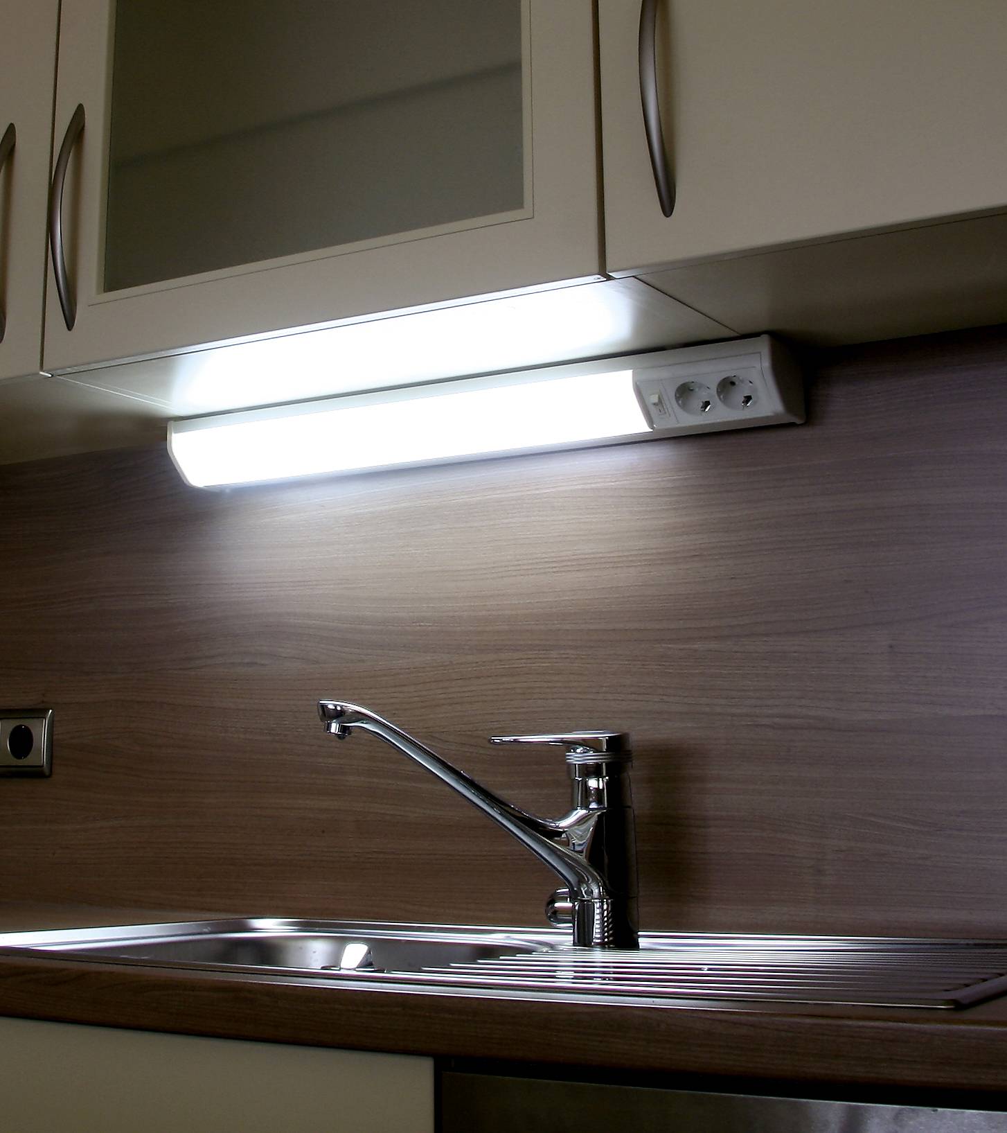 Plan de travail de cuisine avec évier en acier inoxydable et robinet moderne, avec un luminaire encastré au-dessus, assurant un éclairage optimal.