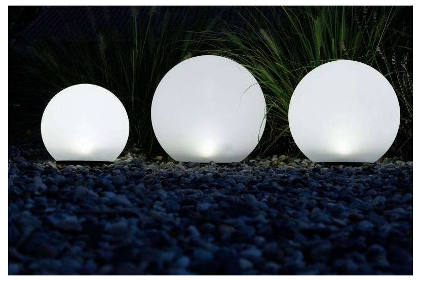 Trois lumières sphériques blanches et brillantes parmi des rochers sombres et de l'herbe haute la nuit.