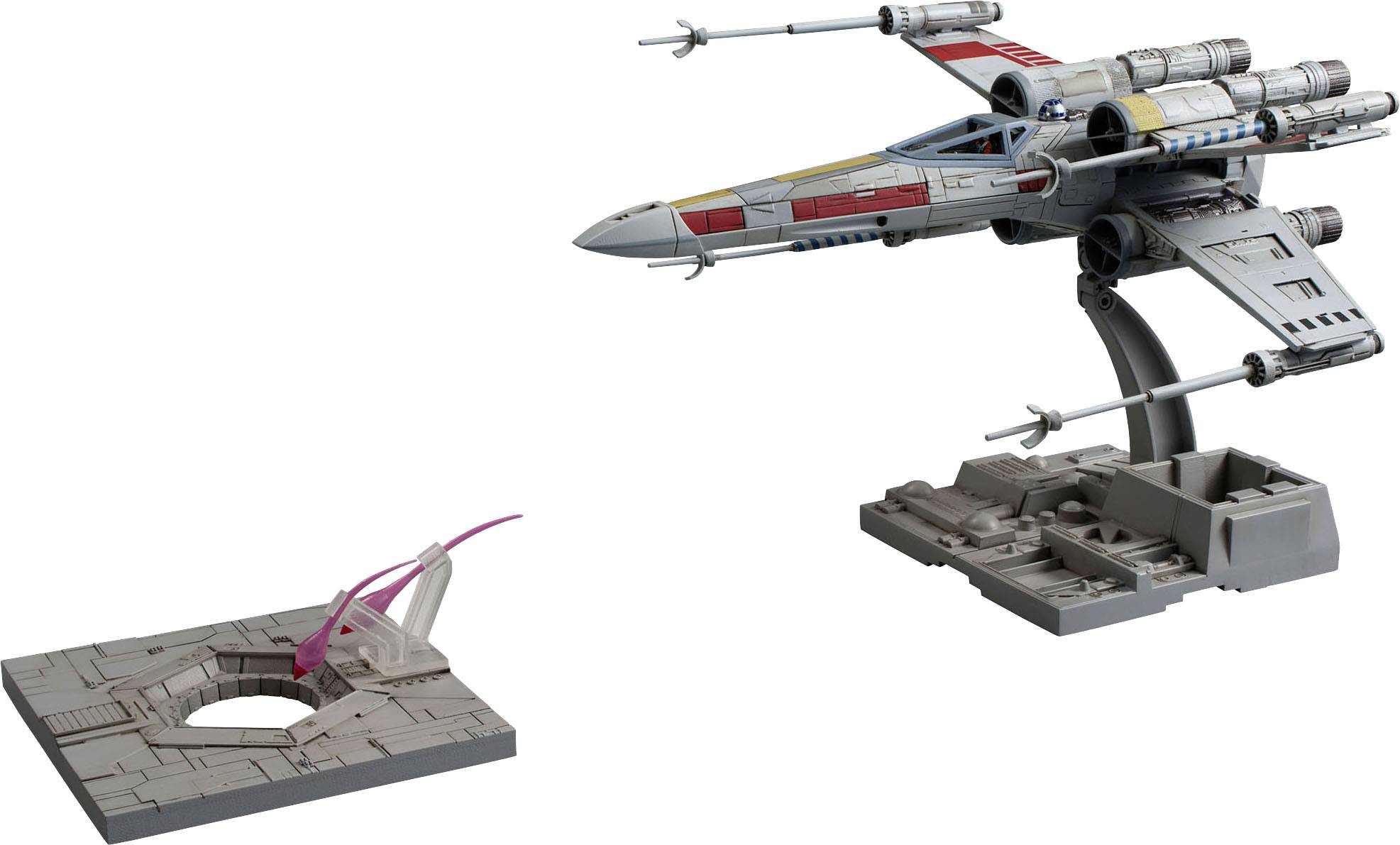 Un modèle détaillé d'un véhicule spatial futuriste aux ailes en forme de X, posé sur un support de présentation à côté d'une rampe de lancement.