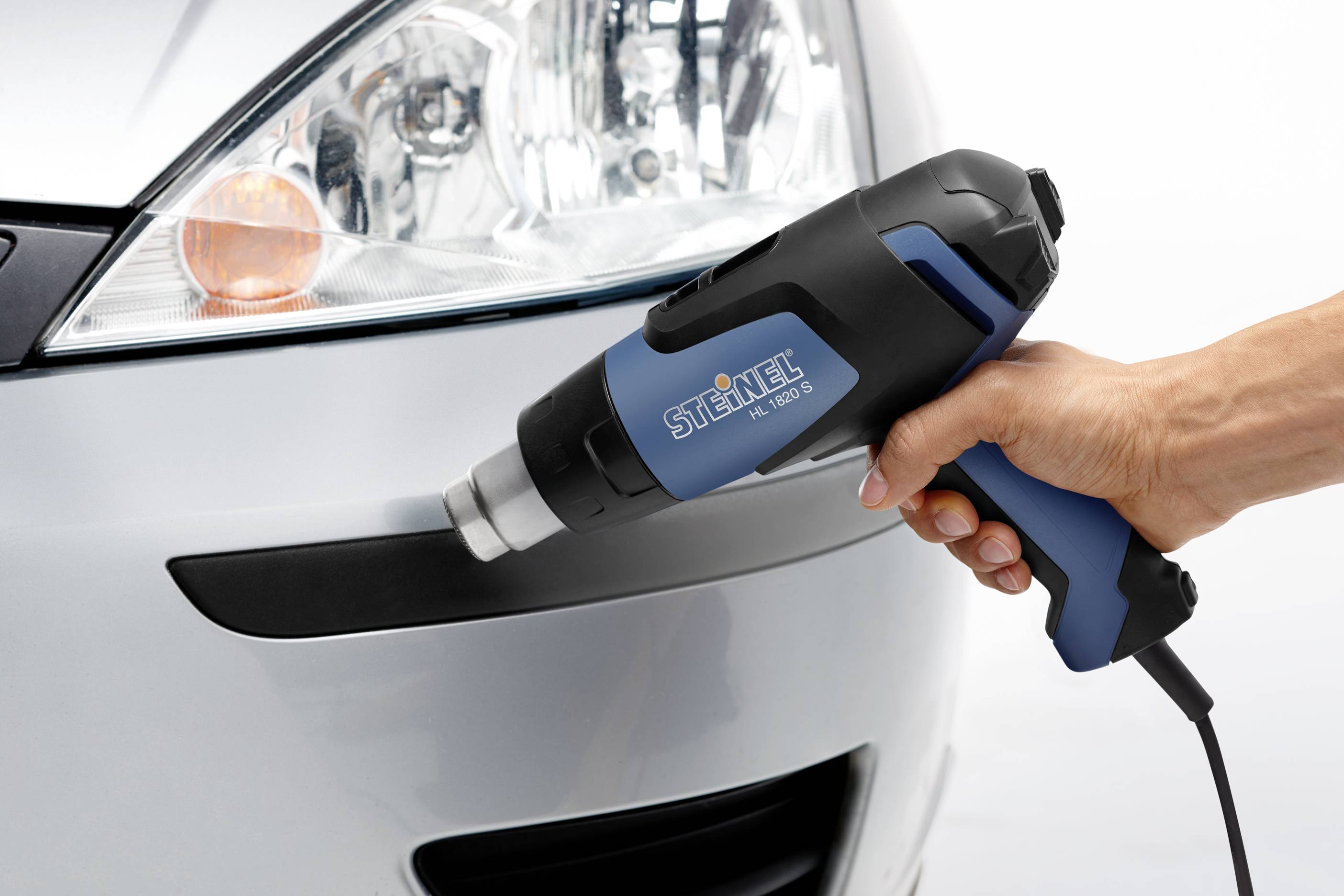 Une main tient un pistolet à air chaud près d'une voiture pour façonner un pare-chocs en plastique.