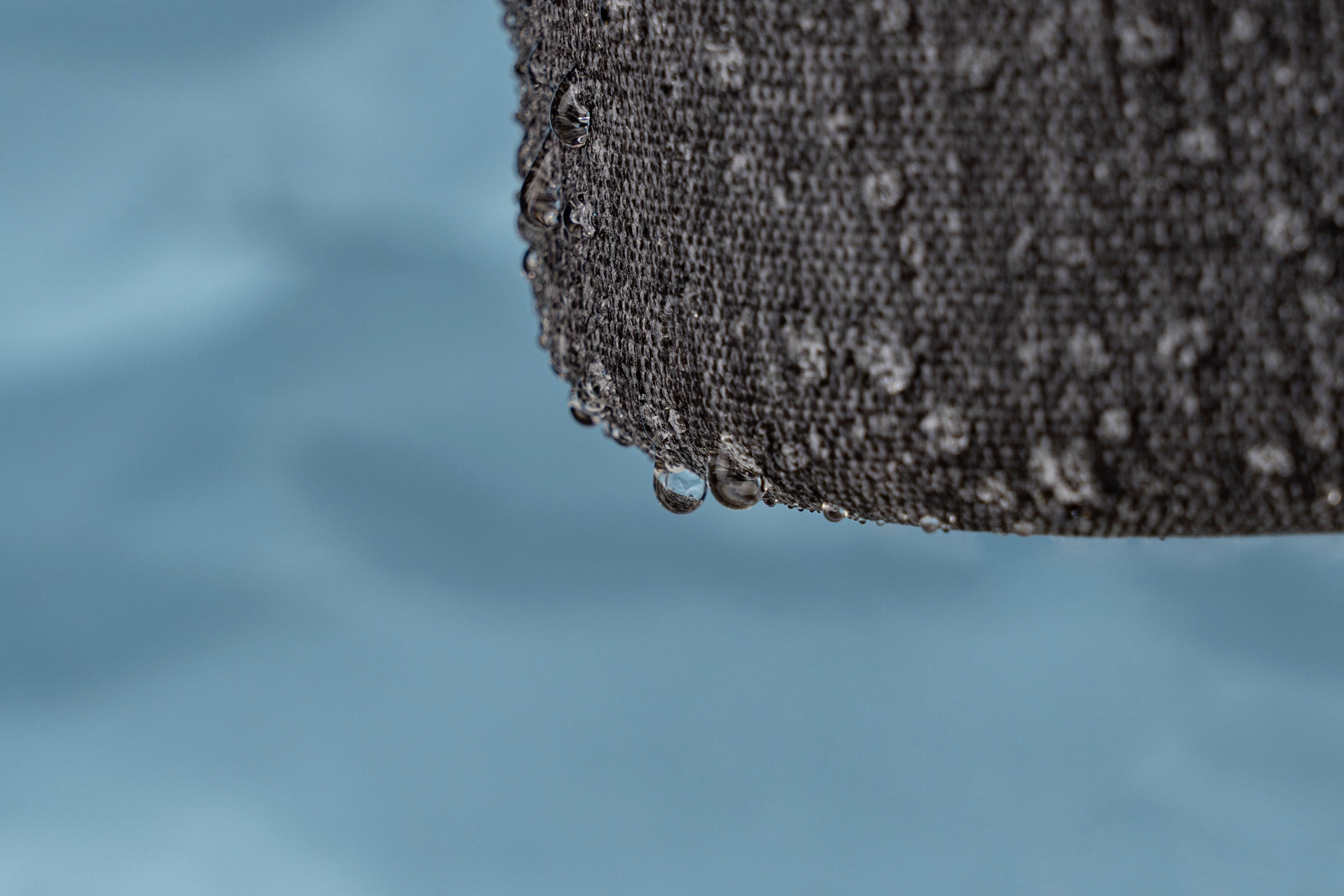 Des gouttes d'eau tombent d'un tissu humide et gris, avec un arrière-plan bleu flou en arrière-plan.